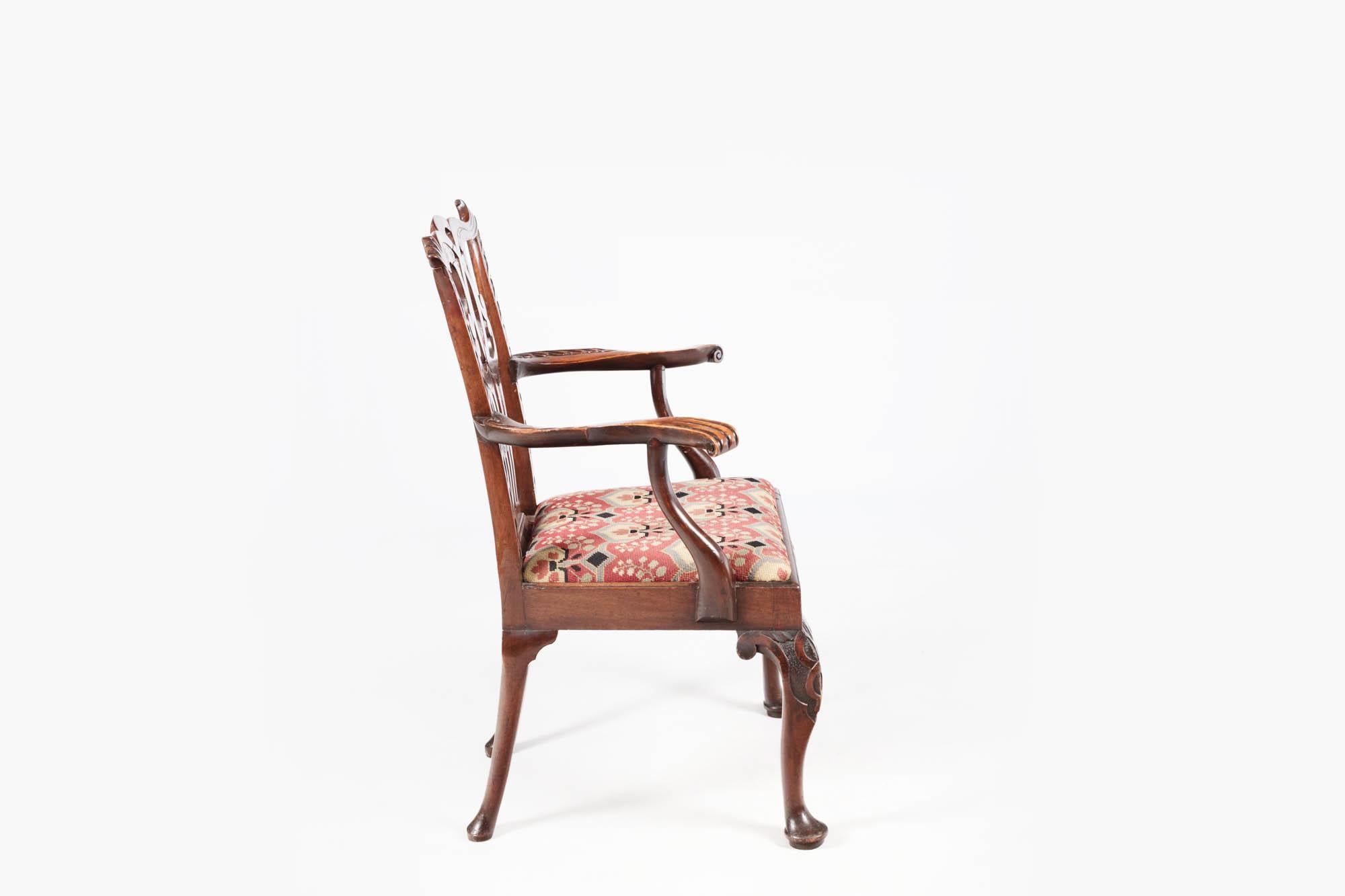 Pair of Chippendale-style carver chairs with drop-in needlework embroidered seats, pierced splat backs and cabriole legs terminating on simple pad feet. This pair of carvers feature outcurved arms with downswept supports. The serpentine top rail