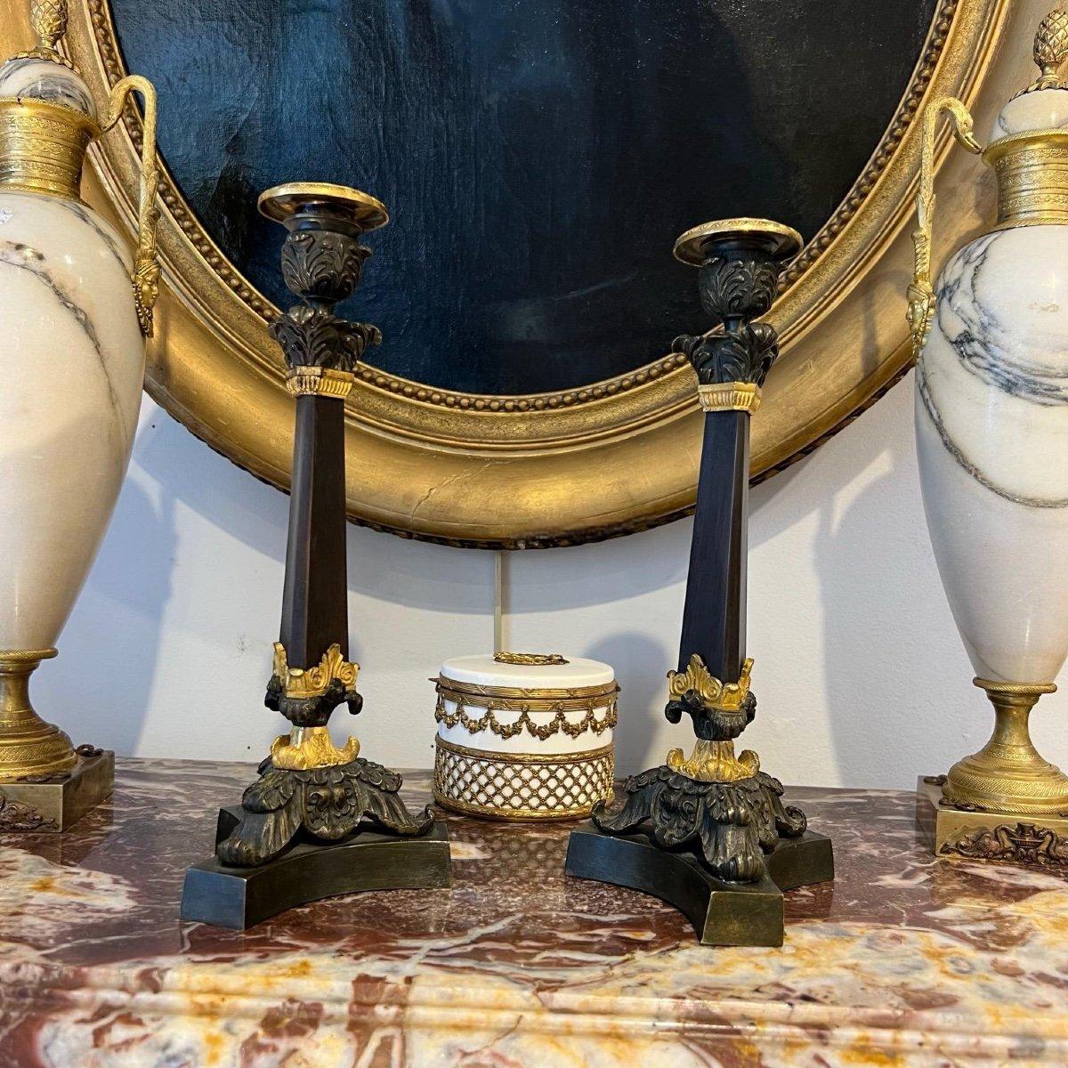 We present you with this rare pair of candlesticks in double patina from the 19th century period of the Bourbon Restoration in France. The brown-patinated stem with a three-sided chamfer at the top adds a distinctive touch to the shape of each