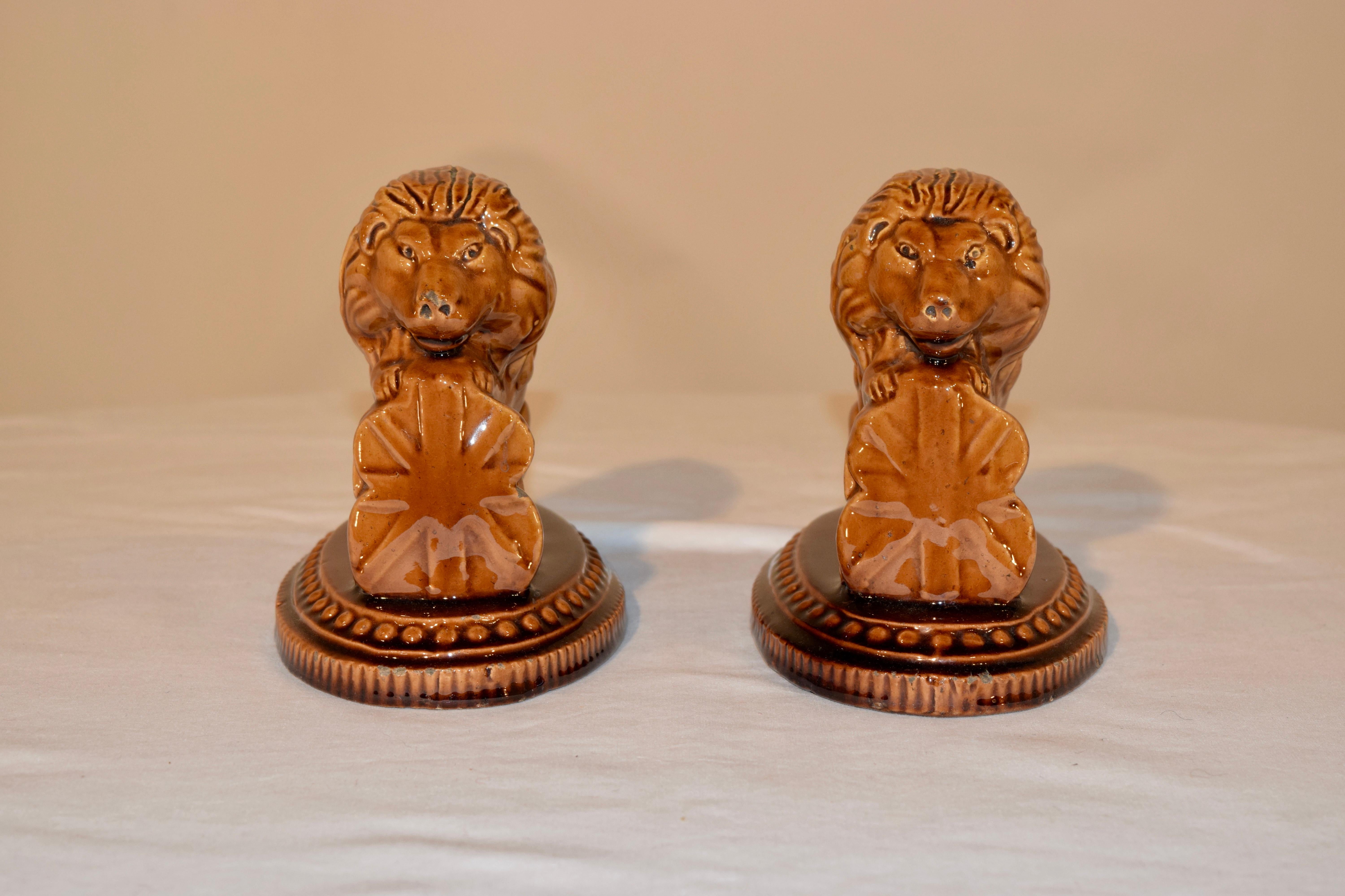 19th century pair of pottery figures of lions resting on English shields. They are sitting on molded bases which are beaded around the platforms. Wonderful color. No maker's mark.
