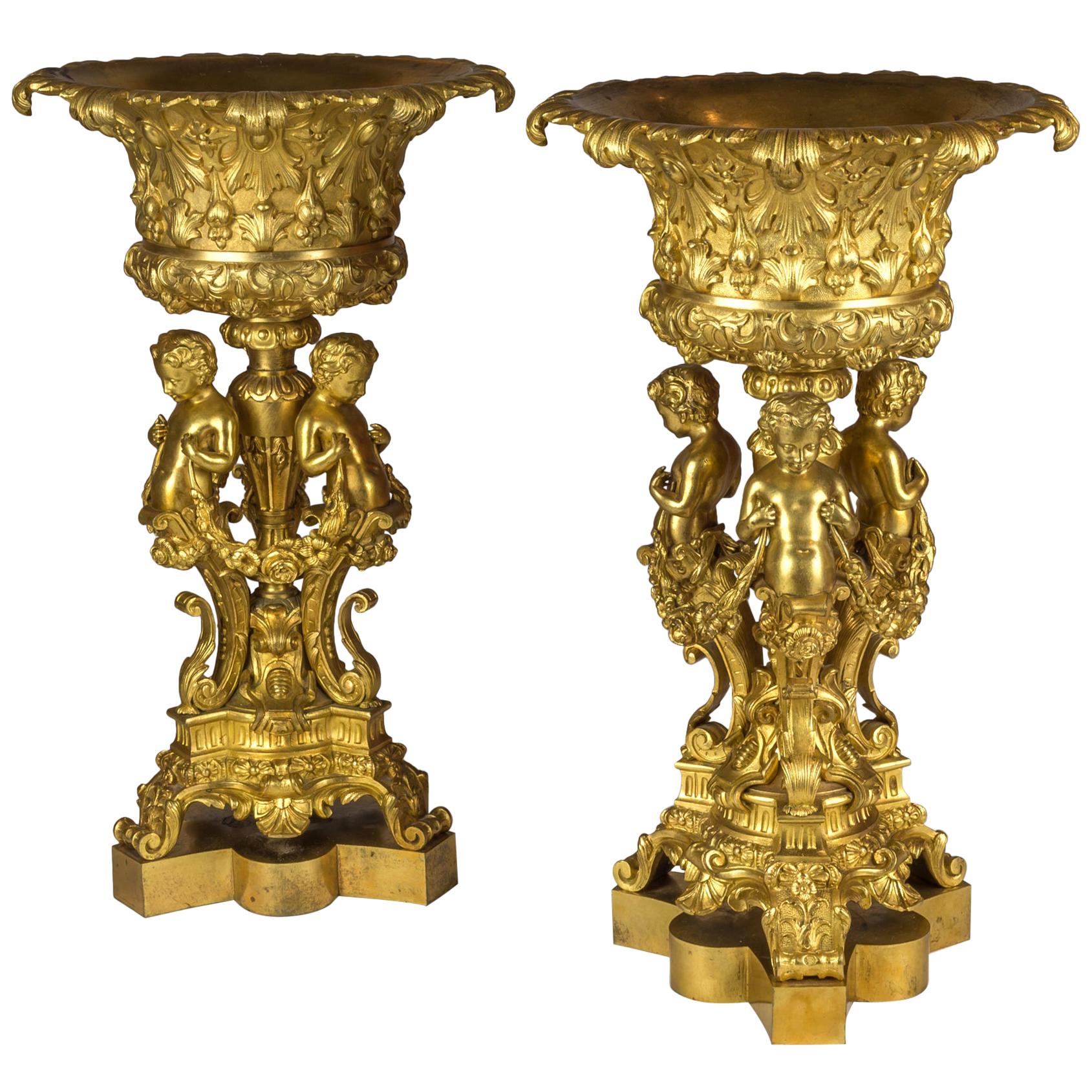 Paire de tazzas figuratifs en bronze doré soutenus par trois chérubins