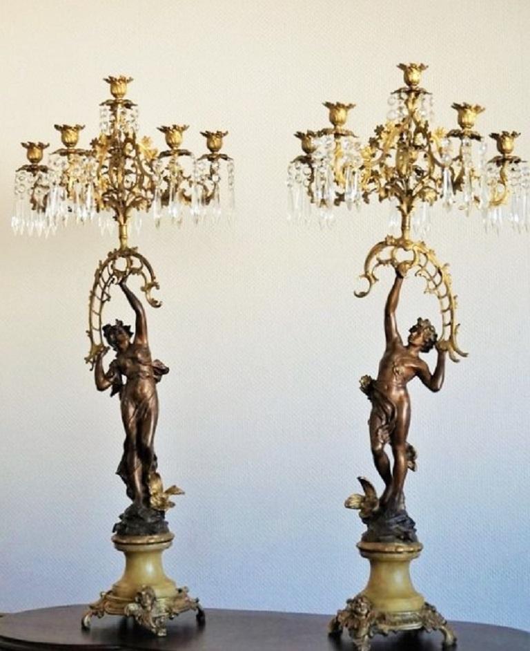 Pair of Empire style patinated and doré bronze figurines male and female candelabras, France, circa 1860-1870. Raised on a monumental marble plinth with doré bronze ormolu-mounted base decorated with angel ornaments. Bronze doré six-light candle