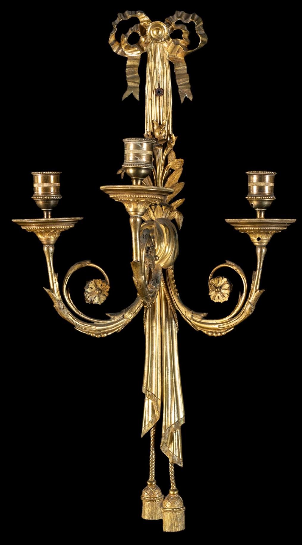19th century, pair of French gilt bronze three-light sconces

This elegant pair of wall lamps was made in France in the early 19th century.
The wall lamps are in gilded bronze finely chiseled in the Louis XVI style. The central covering appears