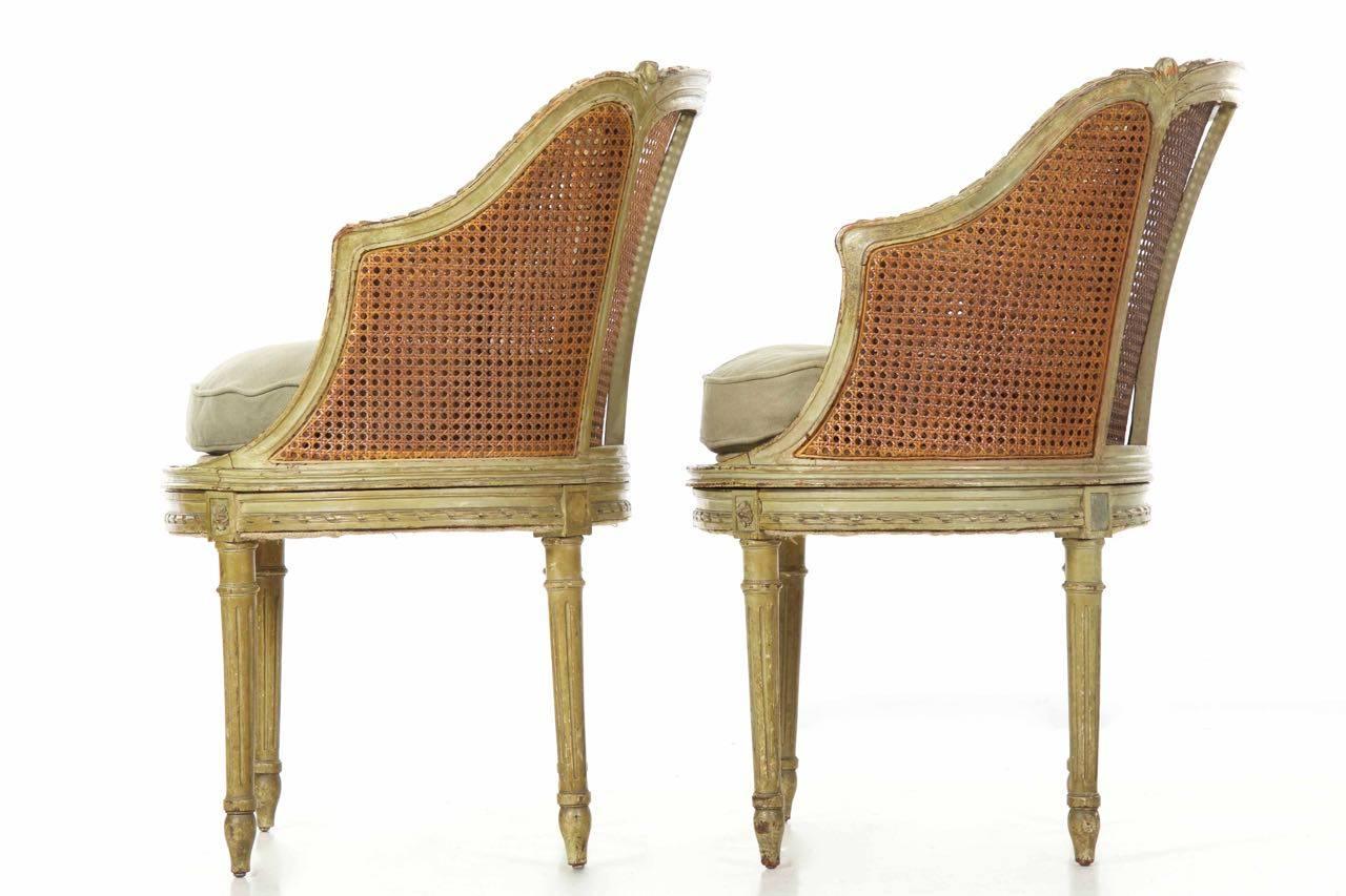 This is a very attractive pair of worn and beautifully patinated Louis XVI style roundback armchairs in at least mostly original forest green paint. The frame is crisply carved and glows in a range from ruby to cognac in the areas where the paint