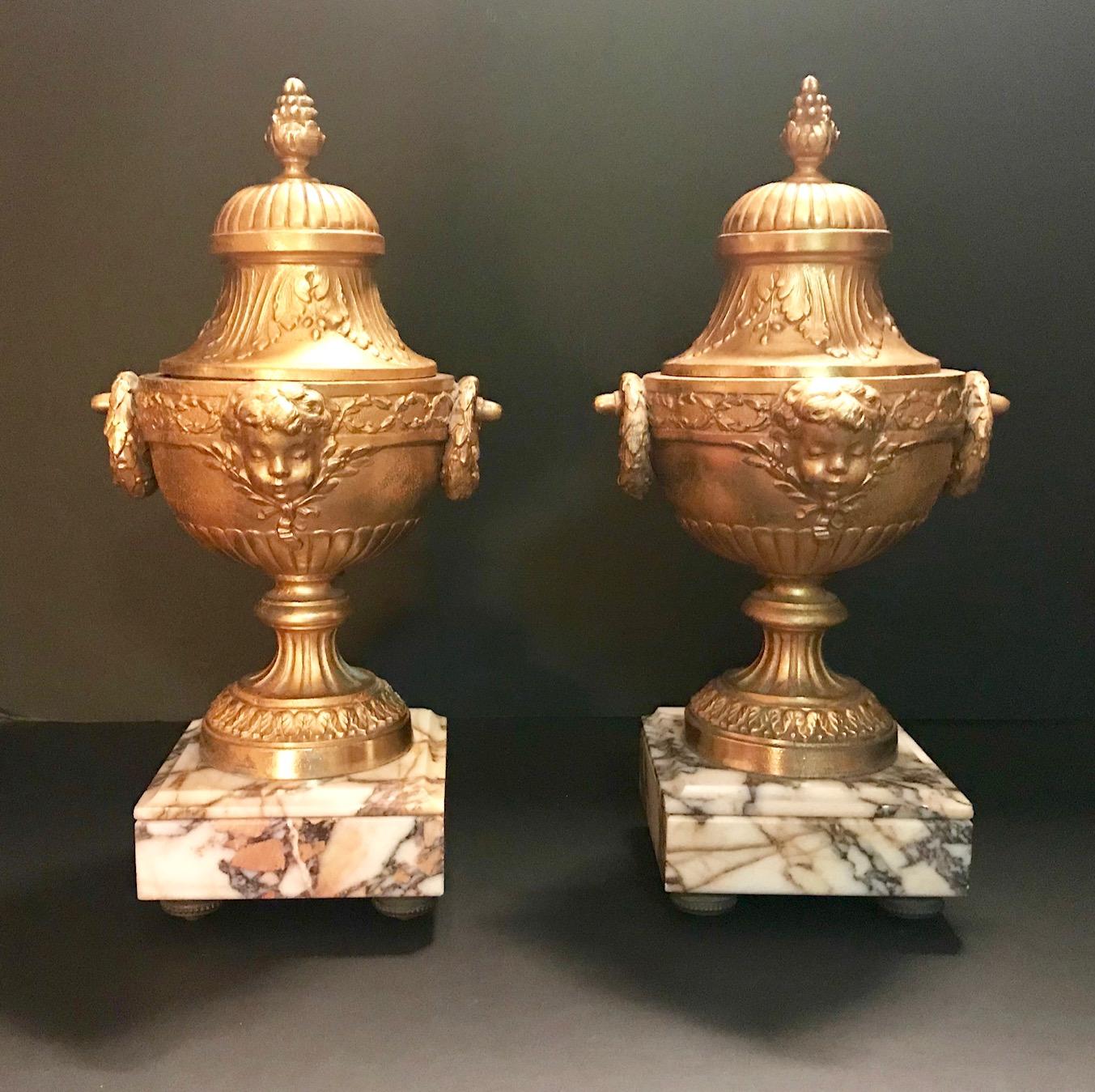 This is a magnificent pair of 19th century gilded bronze urns with highly decorated lids. Two finely detailed laurel wreaths serve as handles on each side while the front center is decorated with a beautiful putto face. The body is adorned in