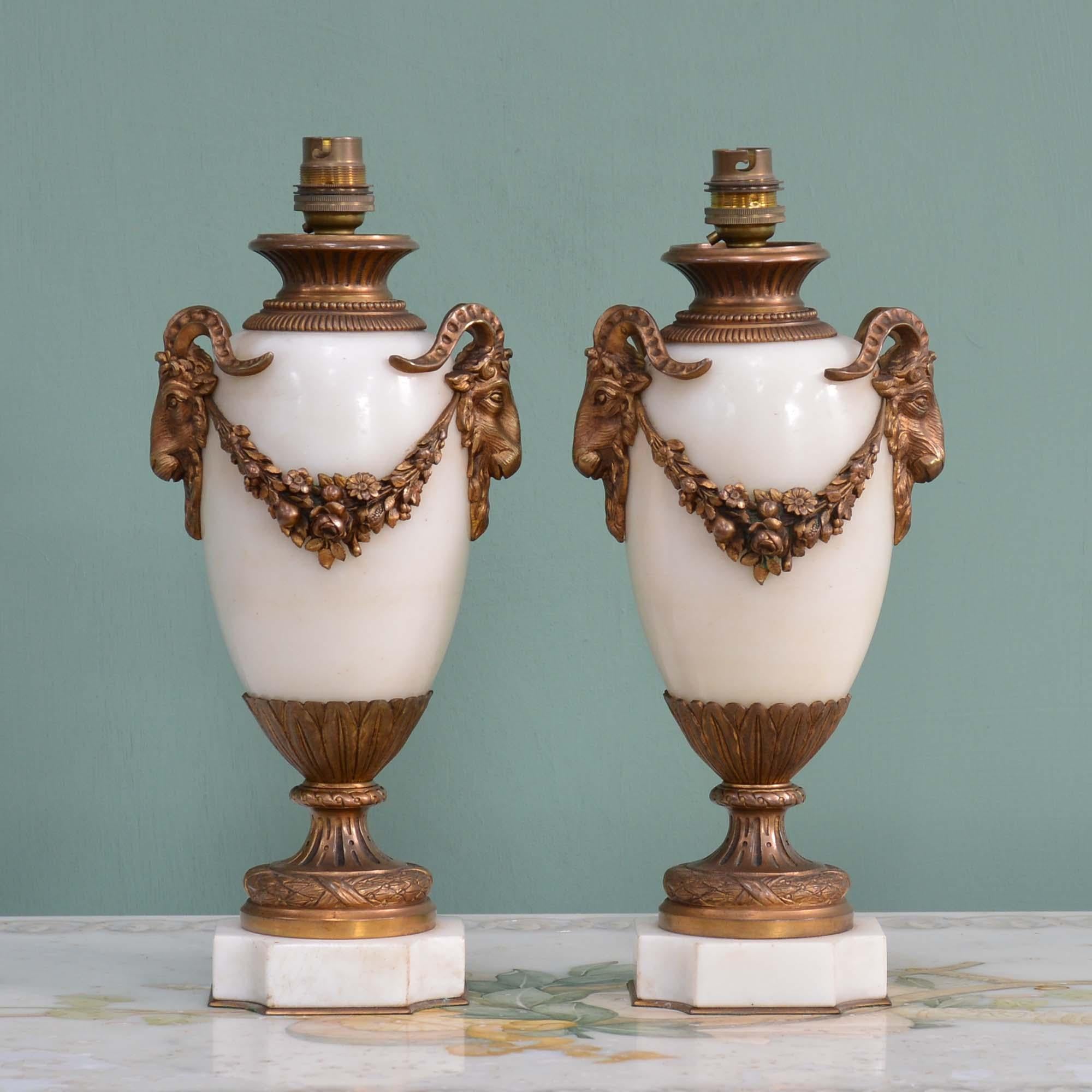A Pair of French Marble Urn Lamps
White marble urns decorated with gilt bronze goats head masks and foliate swags.  Wired for UK and PAT tested.
French, circa 1890

30cm H (to top of urns), 15cm W, 14cm D.

Provenance:
Jardine Hall, Applegirth,