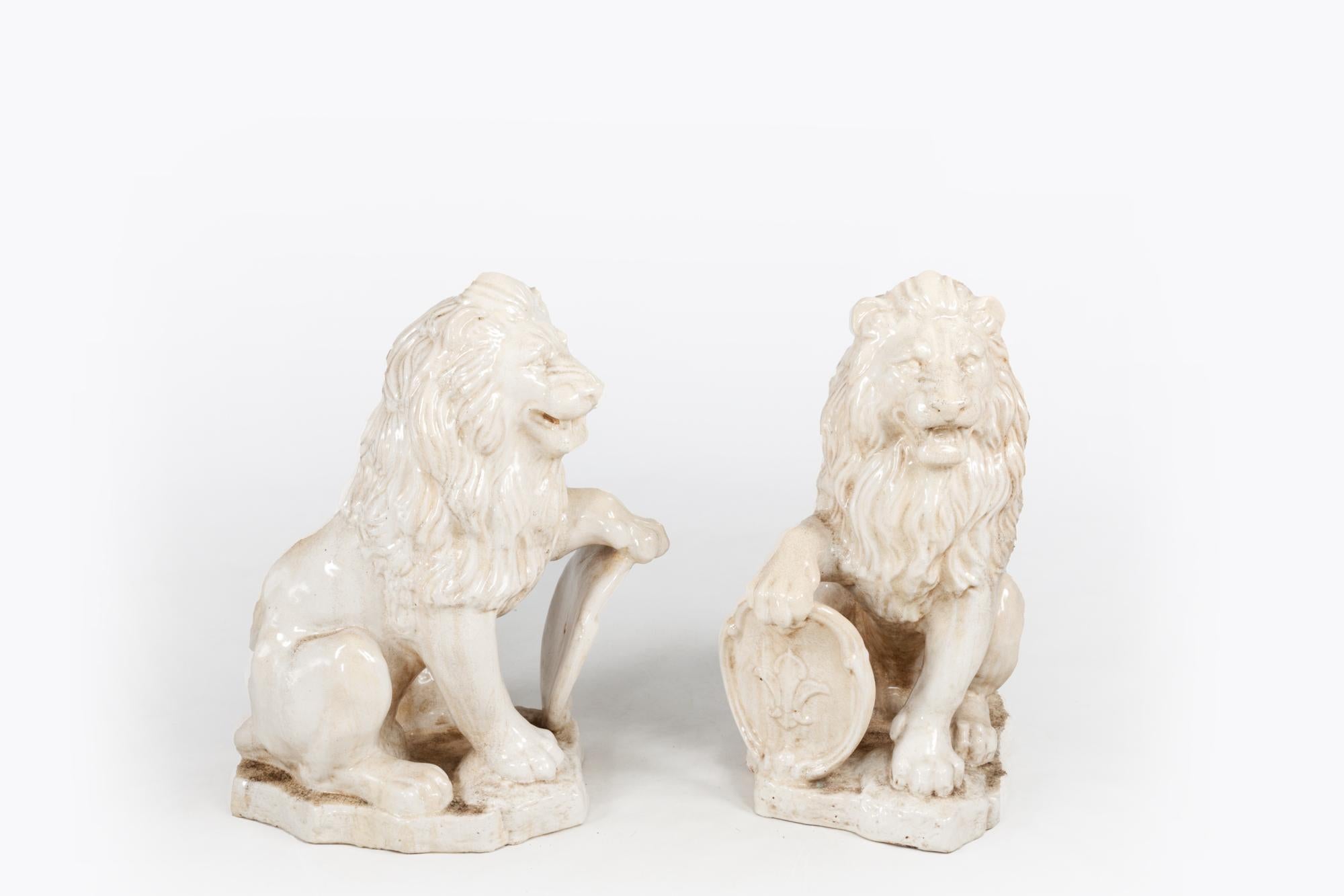 Mid-19th century pair of French painted and glazed terracotta lions grasping oval Fleur De Lis shields while resting on shaped plinths. Circa 1840.

Sculptures of lions were often found in homes in the 18th & 19th centuries, where they were