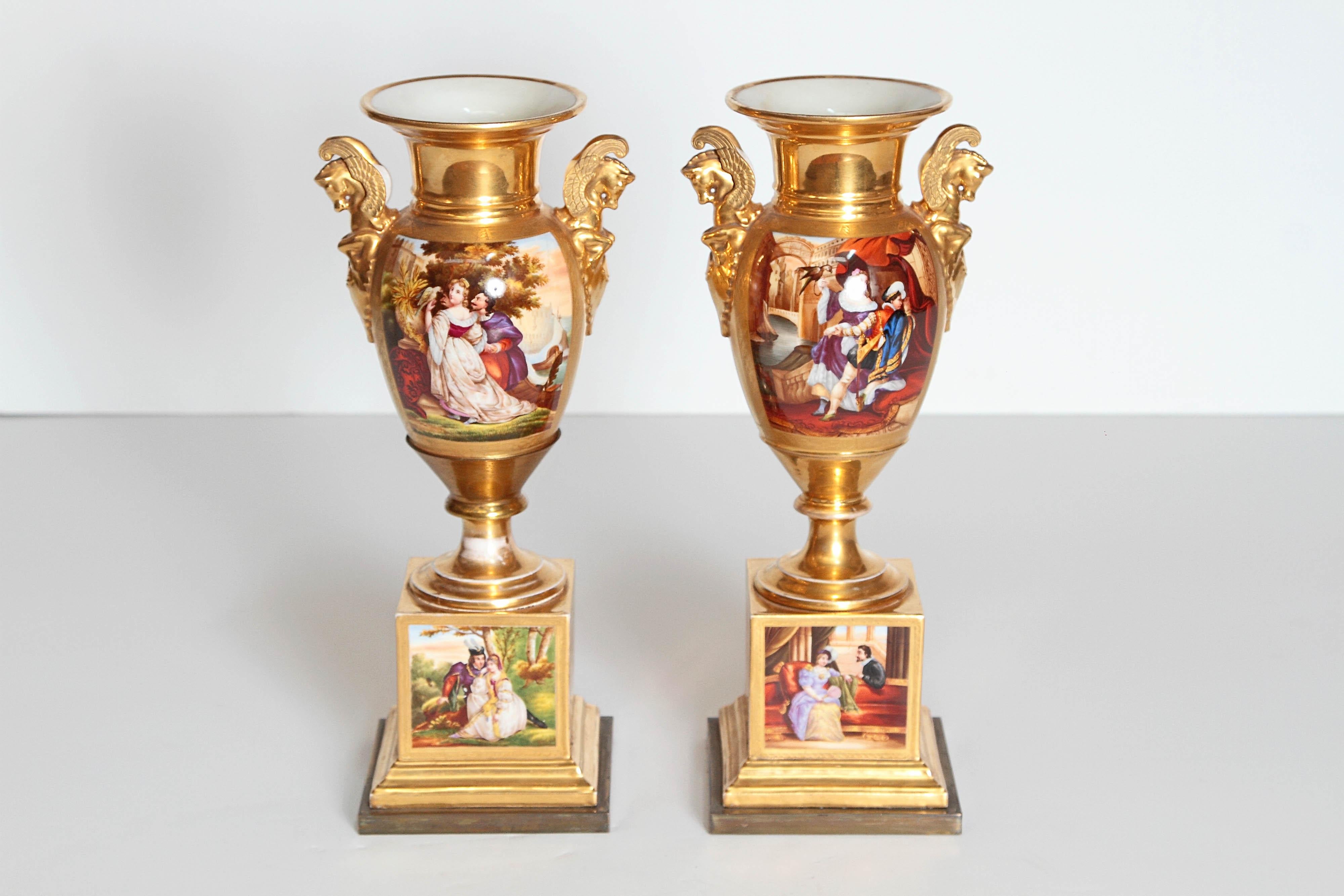 A pair of French porcelain urns, gilt overall with Pegasus busts on sides. Painted panels on side and base with painted scenes on square bases. 19th century, France.