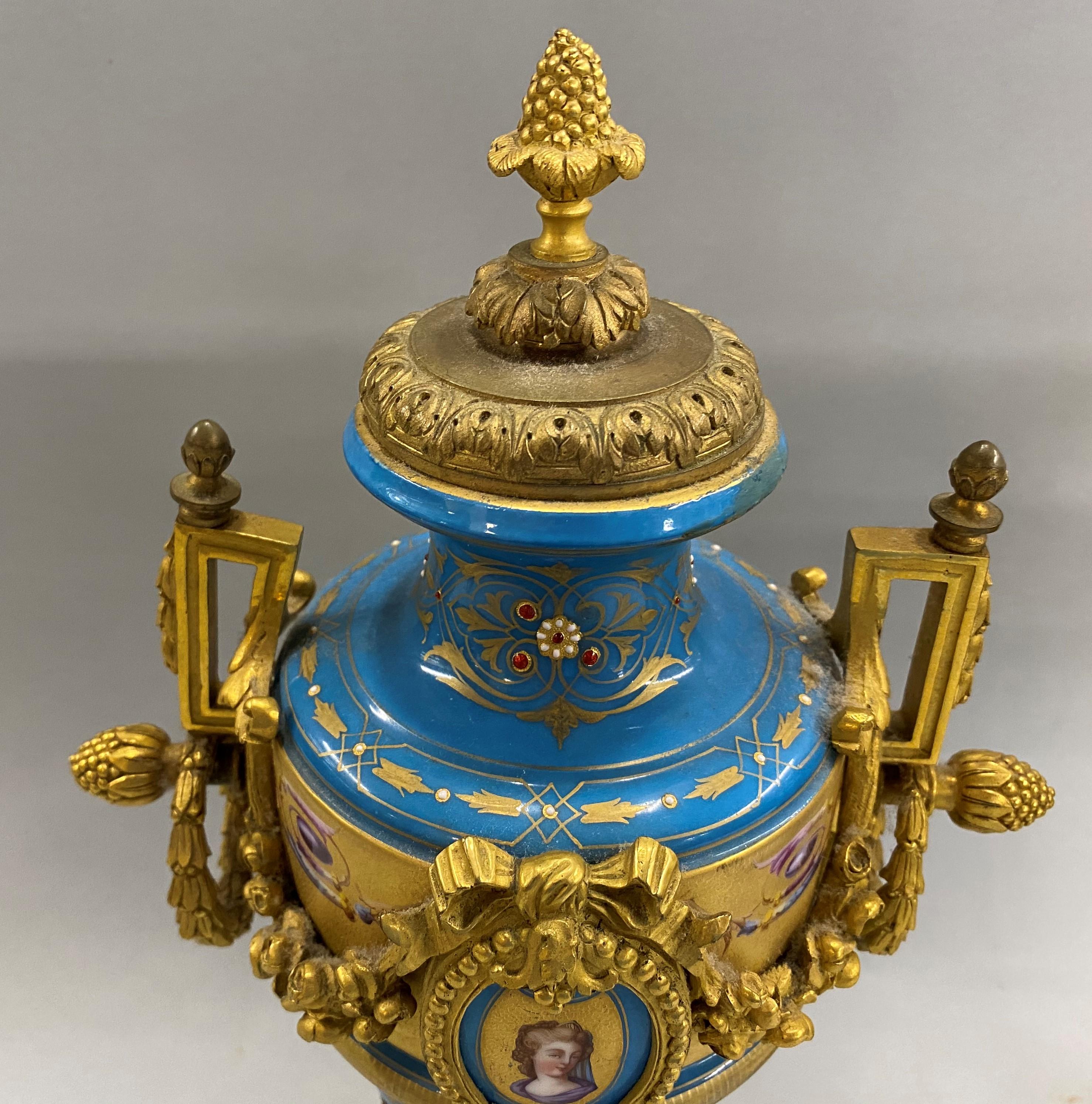 A fine pair of French Sevres Celeste Bleu porcelain urns with a polychrome hand painted oval cartouche on each featuring the bust of a woman, as well as hand painted scrollwork and decorative gilt bronze swag ormolu featuring bellflower wreaths and