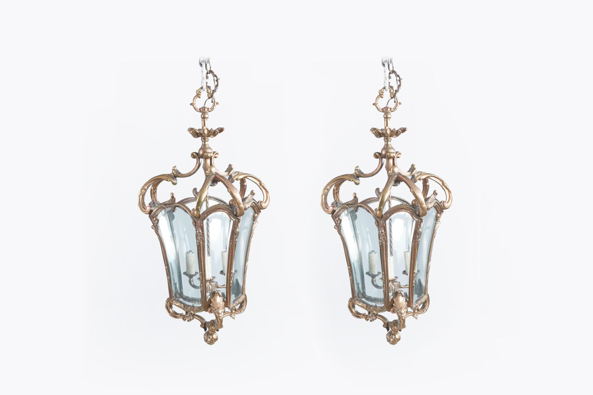 19th Century pair of French style brass hall lanterns with shaped and bevelled glass panels. Featuring ornate C-scroll and acanthus leaf design.