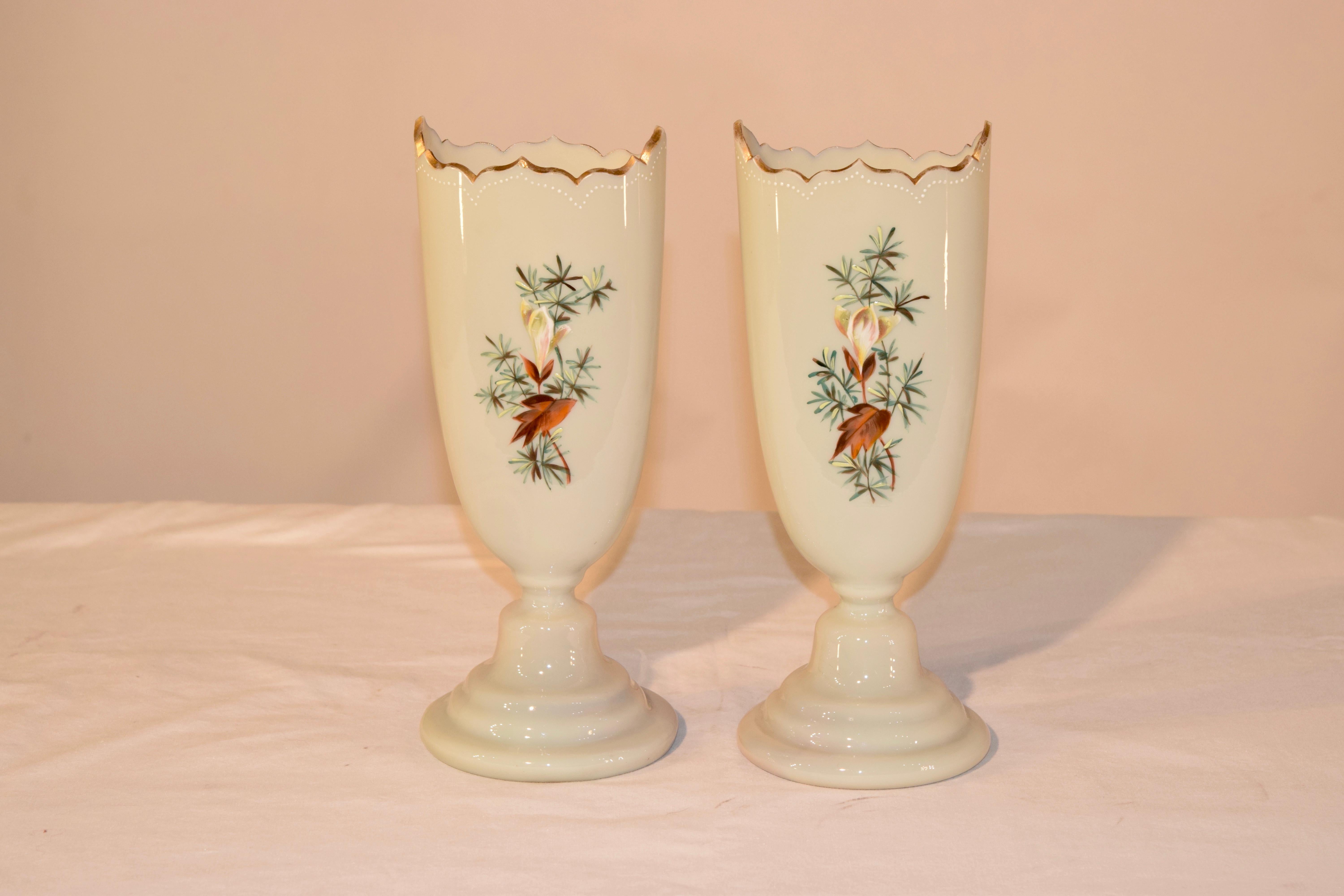 19th century pair of opaline glass vases from France in an unusual shape with a scalloped and gilt edge at the top and wonderfully turned bases. The decoration is hand painted and depicts lovely florals and leaves on the front and back. Beautiful