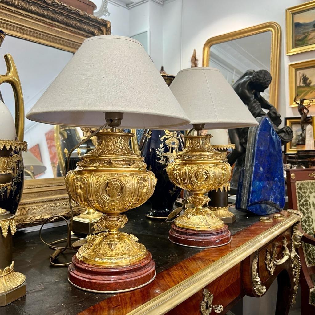 We present a pair of lamps crafted in gilt bronze, featuring a rich and diverse array of decorative elements, including male and female mascaron ornaments, ancient-style musicians, and the heads of lions and rams. The gilt bronze work is of