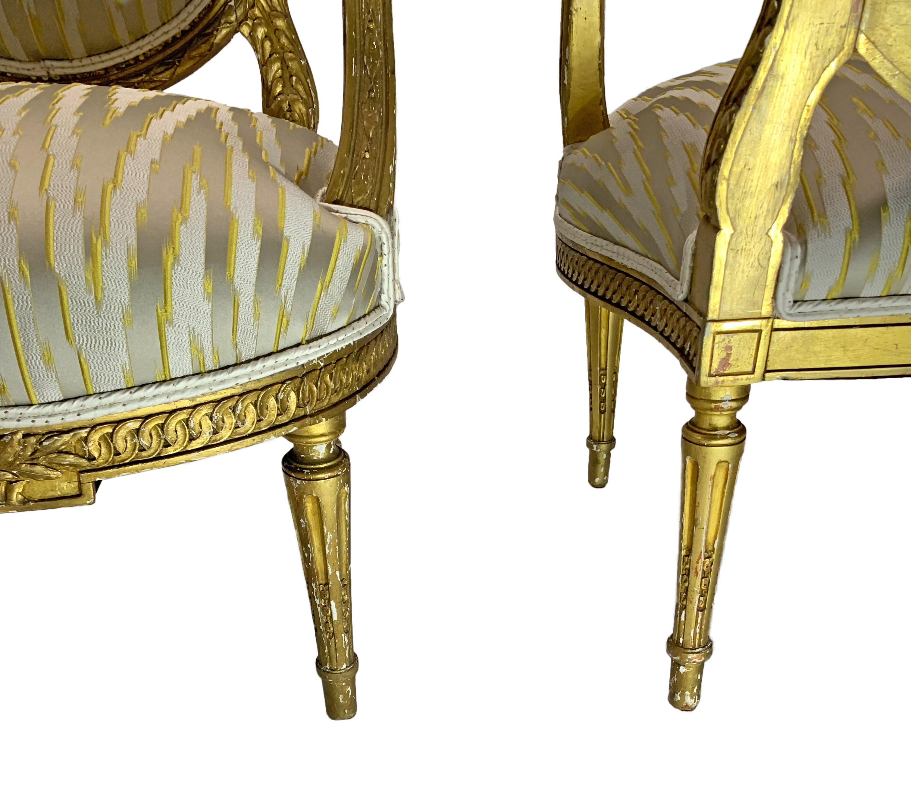 19th century pair of giltwood Louis XVI style French oval back armchairs. These chairs were owned by couple who worked at US Embassy in Paris, France during the 1960s. The chairs are sturdy and have recently been reupholstered in a contemporary