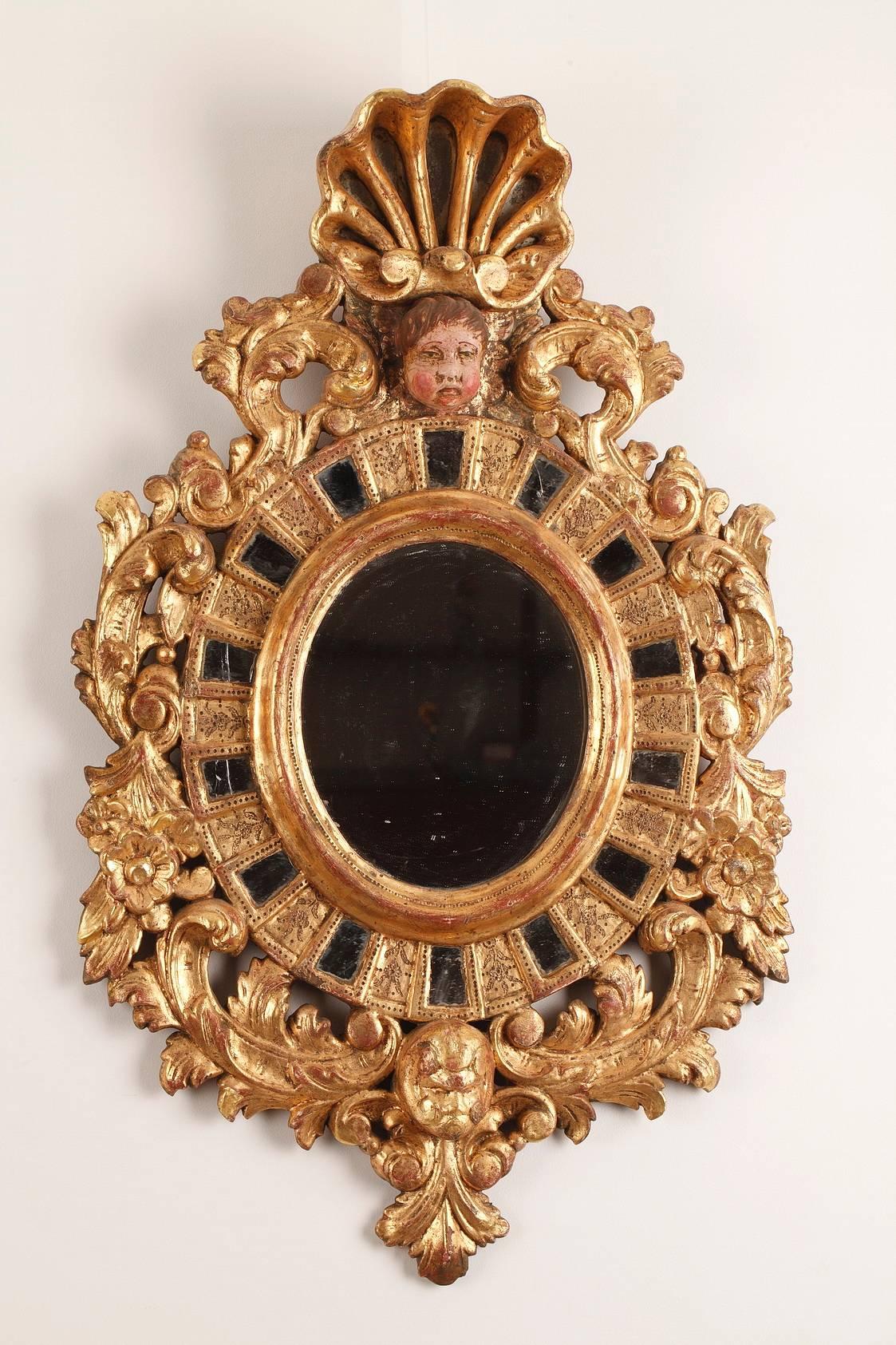 Paire de miroirs en bois doré de la fin du 19e siècle avec incrustations de verre. Ils sont décorés d'acanthes, de fleurs et de feuillages. Le dessus des miroirs est orné de têtes d'anges et de coquillages peints dans le style vénitien du XVIIe