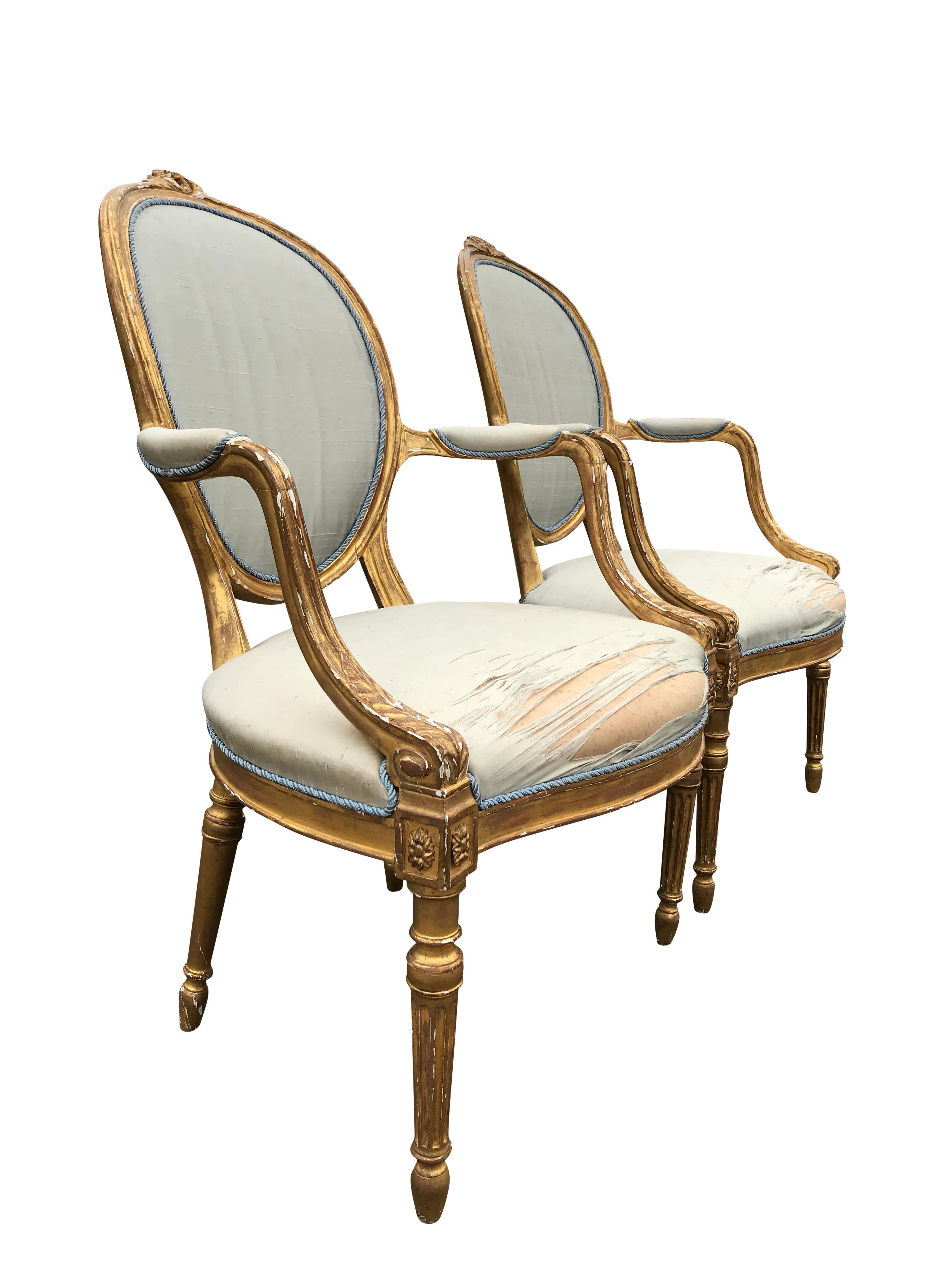Elegant pair of water gilded open armchairs, of generous proportions, in the manner of George Hepplewhite. The silk fabric and frames are elegantly distressed but structurally sound.