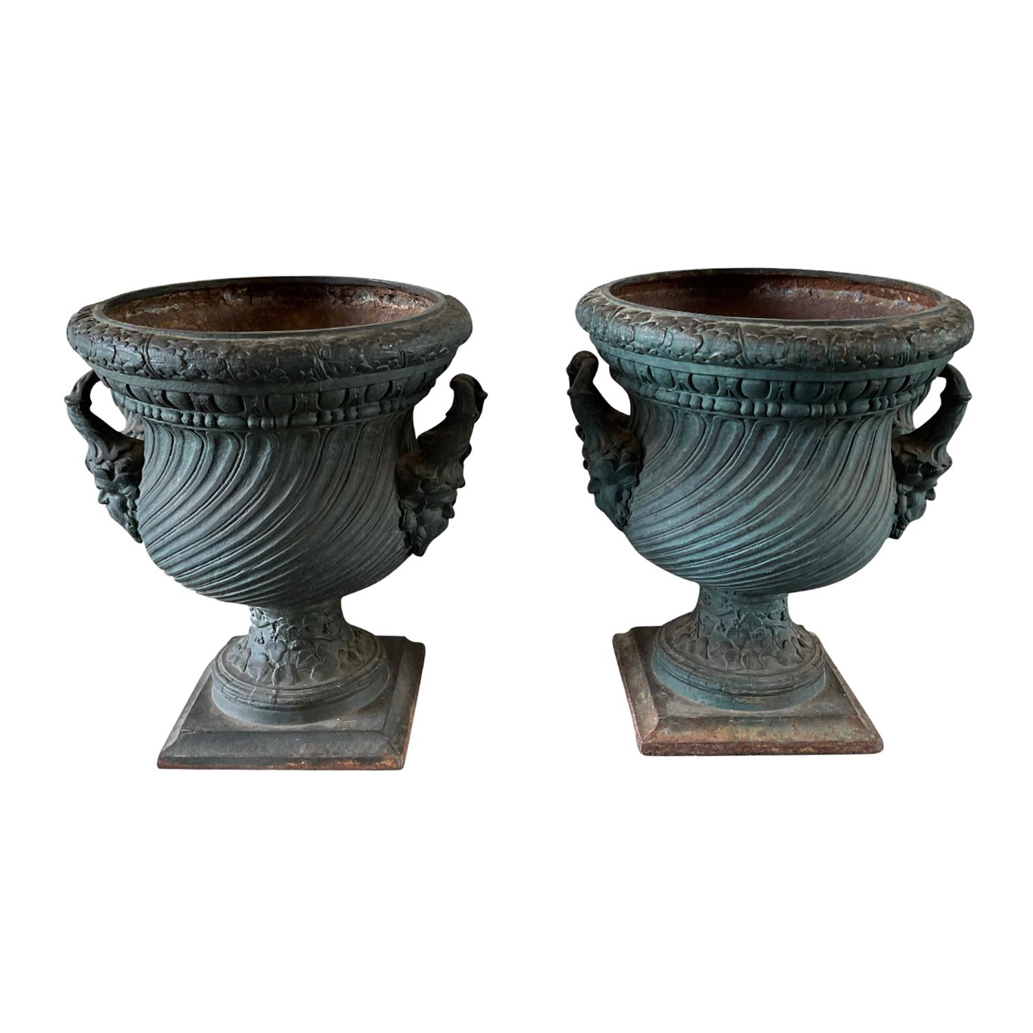 An antique pair of 19th Century heavy garden urns made of hand crafted cast iron, in good condition. The set of French planters are in their raw iron state with few traces of historic paint. The beautifully richly adorned round bodices are flanked
