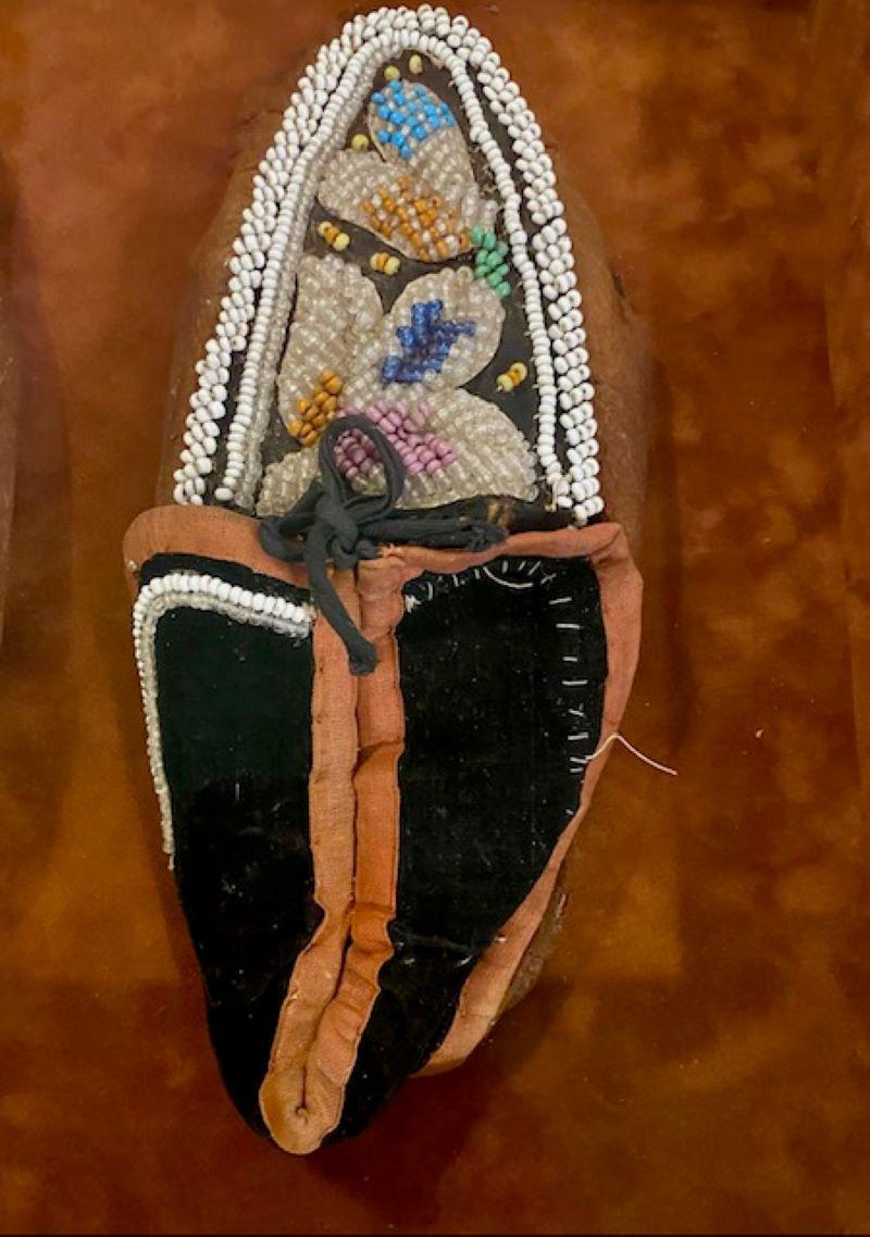 19th Century Pair of Iroquois Moccasins, New York or Ontario, mid to late 19th Century, a worn pair of moccasins with suede bodies, blue trade cloth tops with red trade cloth border, decorated with glass bead floral design and white seed bead