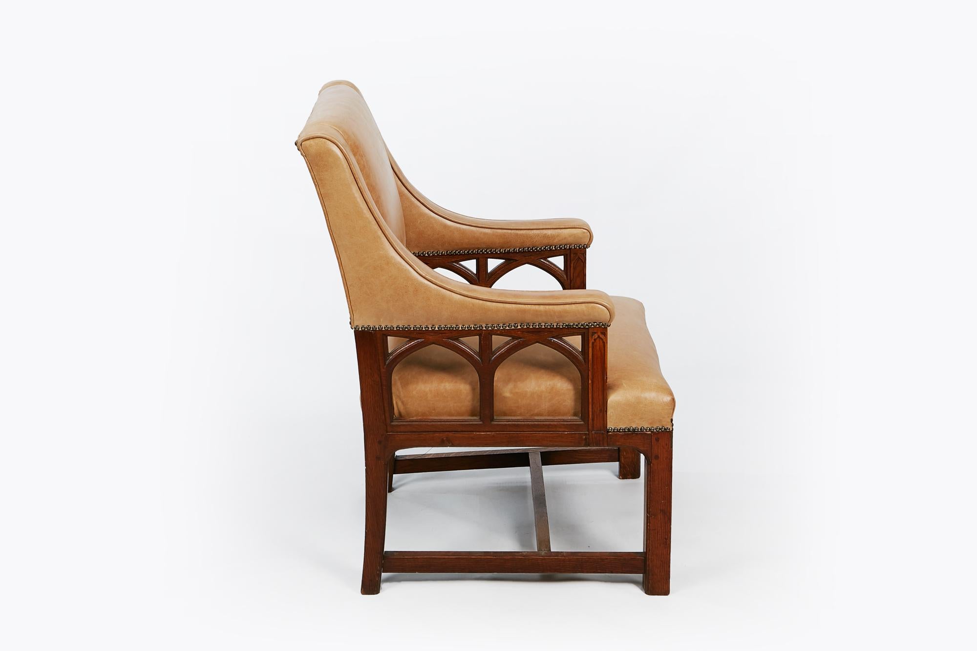 19th century pair of oak library armchairs in the Gothic manner. The rectangular padded upholstered back with down swept padded open Gothic arched supports over stuffed seat raised on square legs joined with H stretcher.