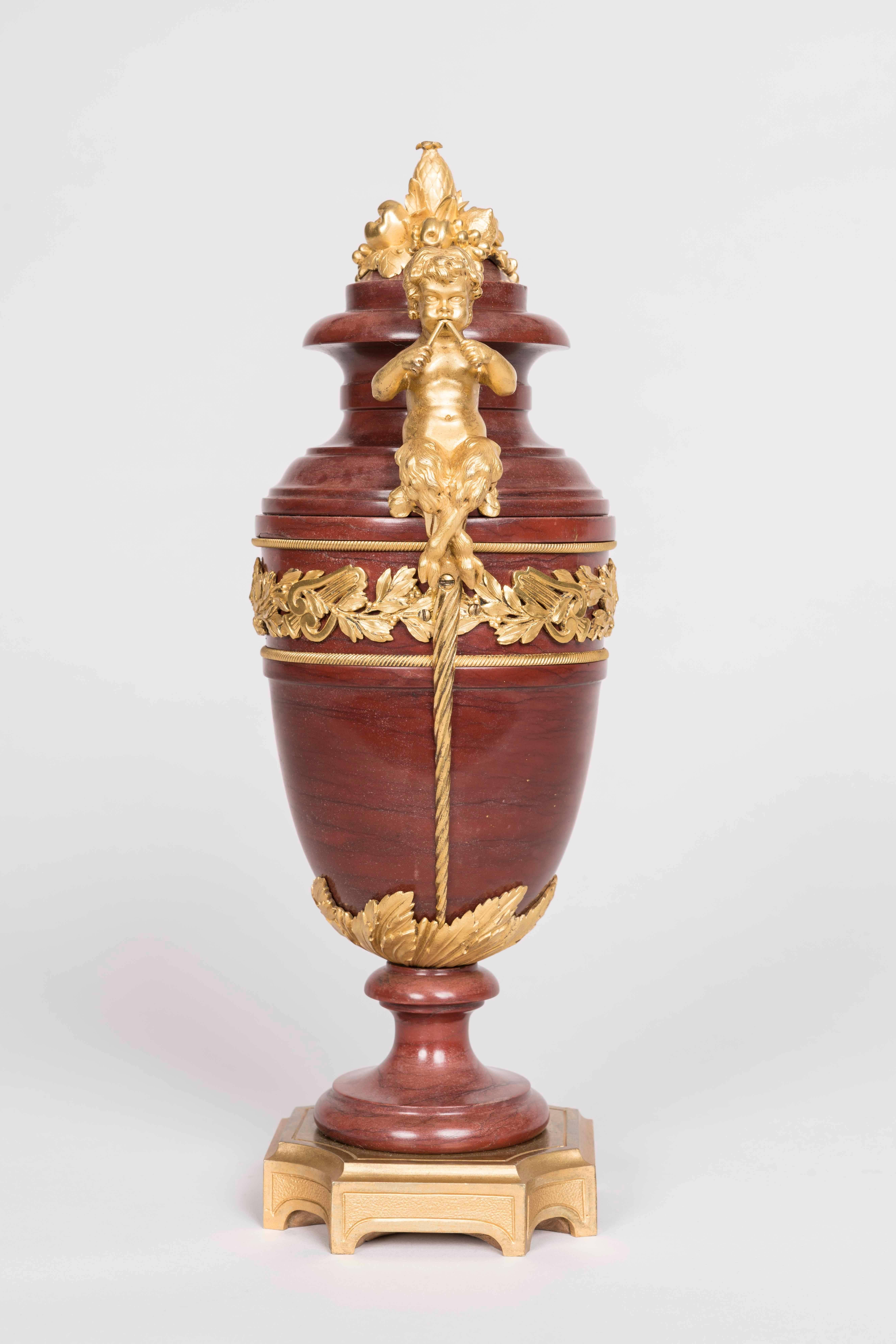 A pair of urns in the Louis XVI manner attributed to Henry Dasson.

Constructed utilising Antico Rosso marble and ormolu; rising from incurved square stepped ormolu bases, the tapering leaf girt ovoid bodies supported by waisted socles, having