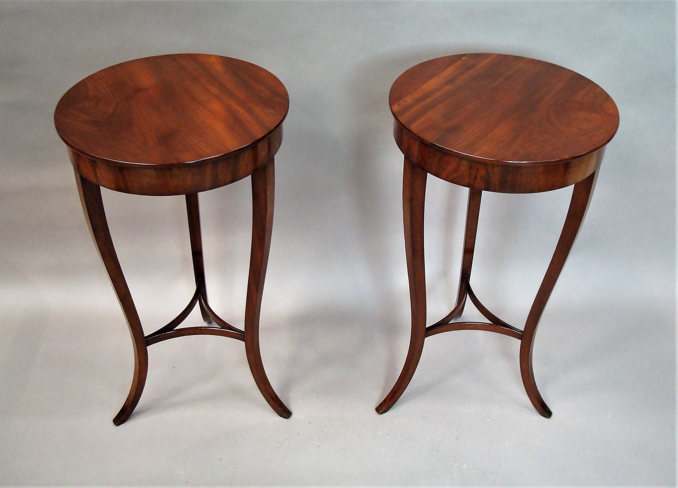 Elegant 19th century pair of mahogany occasional / end tables of stylish design; the well figured circular tops with a slender molded edge above a flame mahogany inset frieze raised on three tapering swept legs united by shaped stretchers. Good