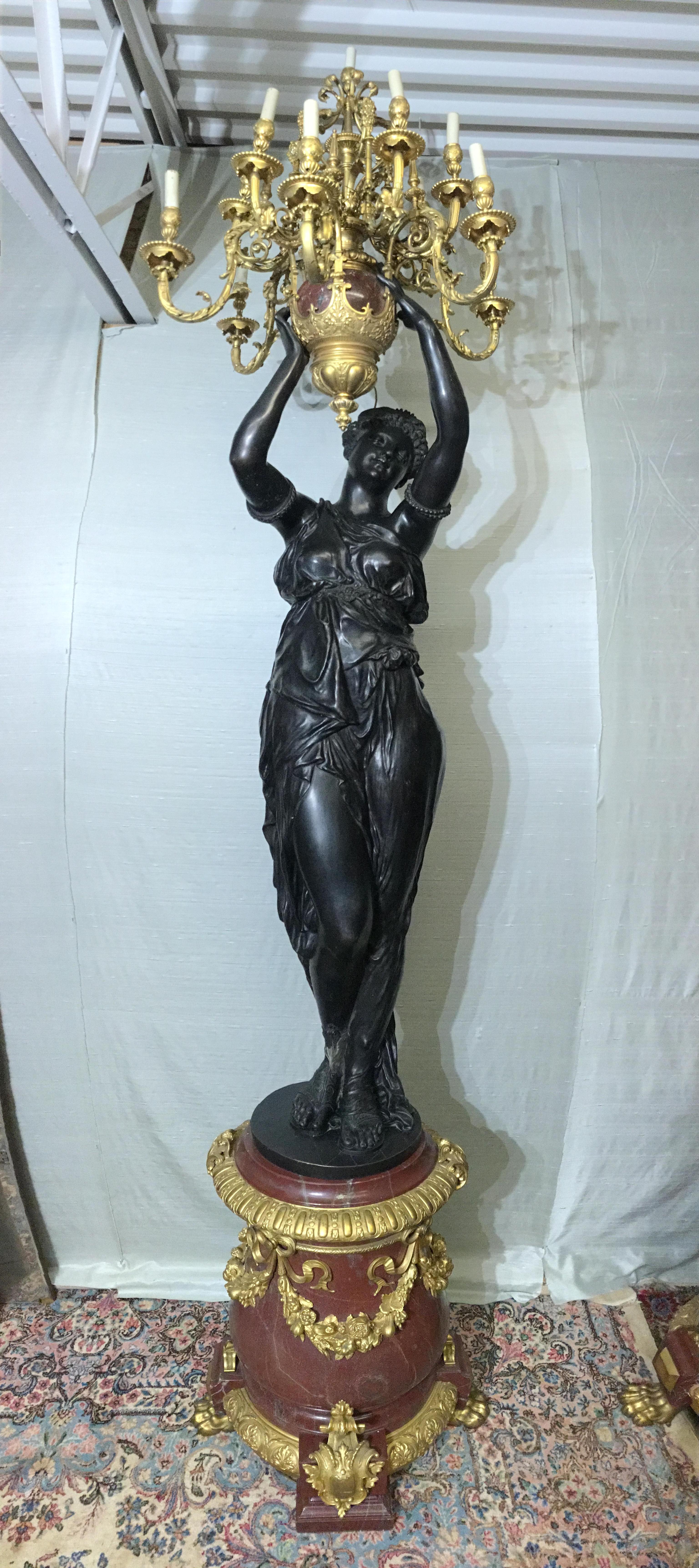 A large pair of French early 20th century patinated bronze and Rouge Griotte marble after Albert-Ernest Carrier-Belleuse (1824-1887), Paris each standing classically draped female figure holding aloft an urn issuing scrolling acanthus branches, each