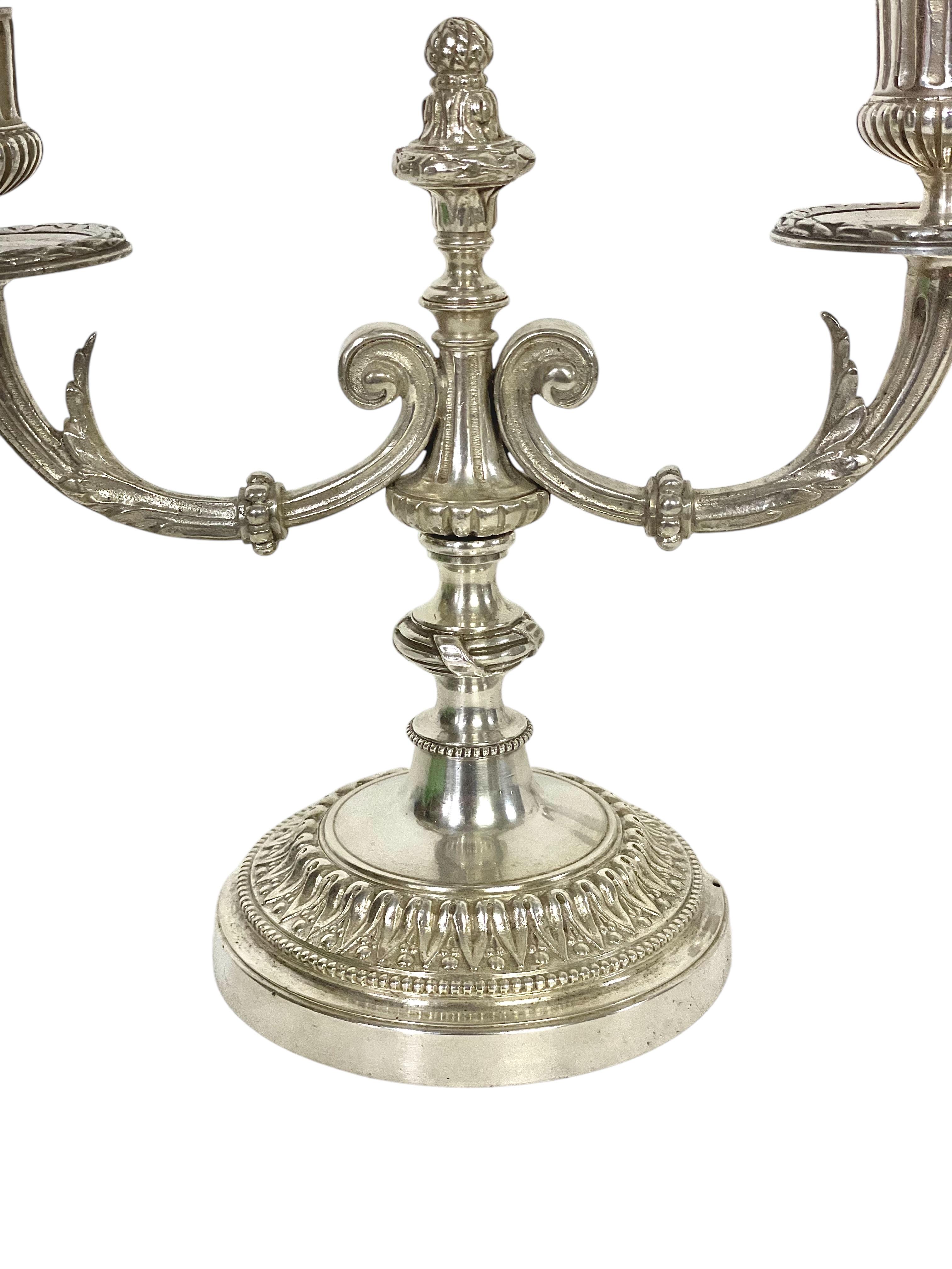Coppia di candelabri argentati in stile Luigi XVI del XIX secolo con due bracci di luce elegantemente ricurvi, perfetti come pezzi d'arredamento da fine tavola. Ogni braccio presenta intricati dettagli scultorei ed è sormontato da bobeches rotonde