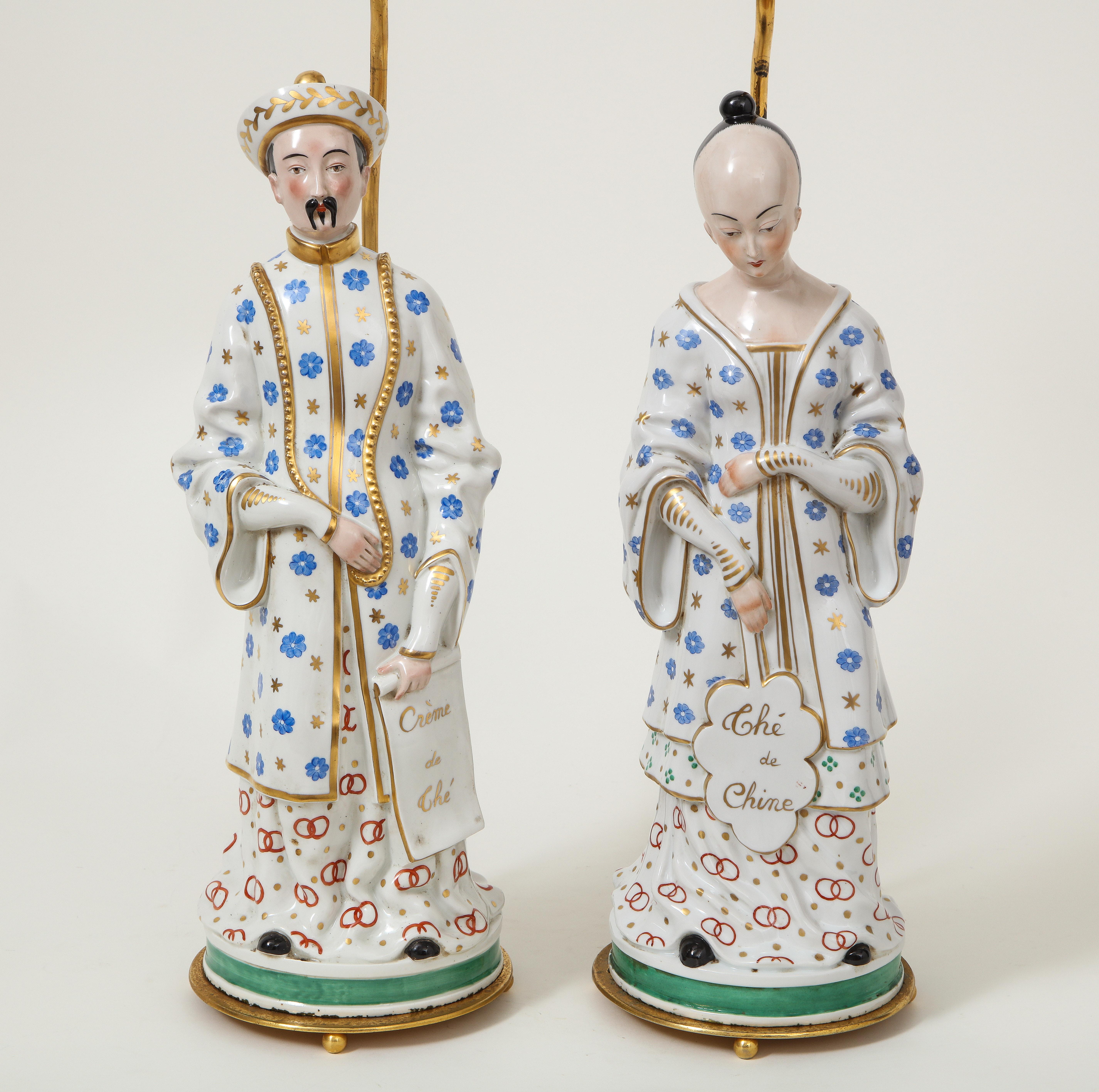 A pair of male and female court figures dress in blue, white and gilt robes, mounted on a gilt bases; the male holding a fan inscribed 