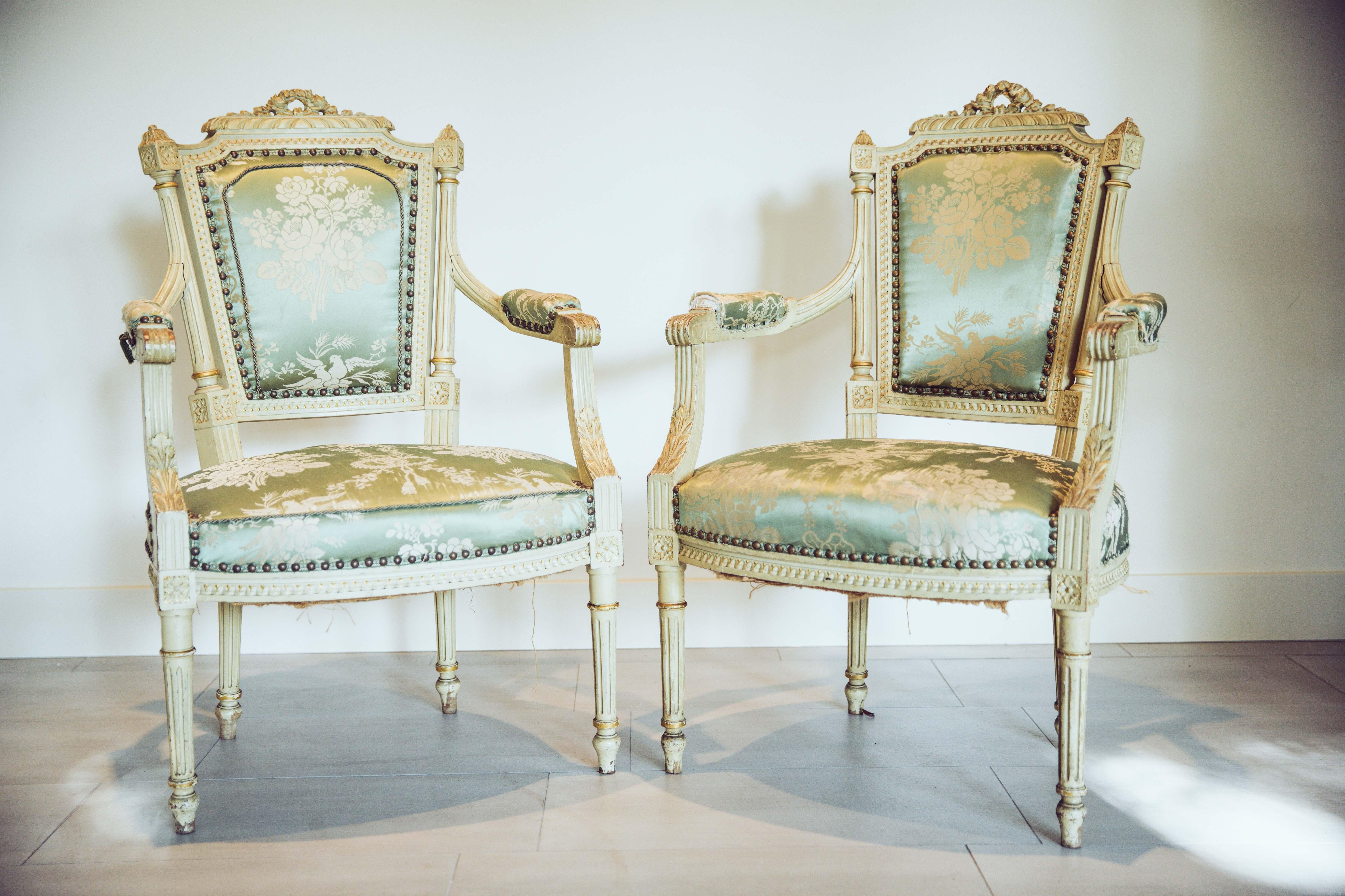 19th century pair of open arm fauteuils in the Louis XVI style. Beautiful original painted finish in a creamy white finish. Lovely carved details along the seat bottom edges, with a Classic Louis XVI fluted legs. The arms have with upholstered arm