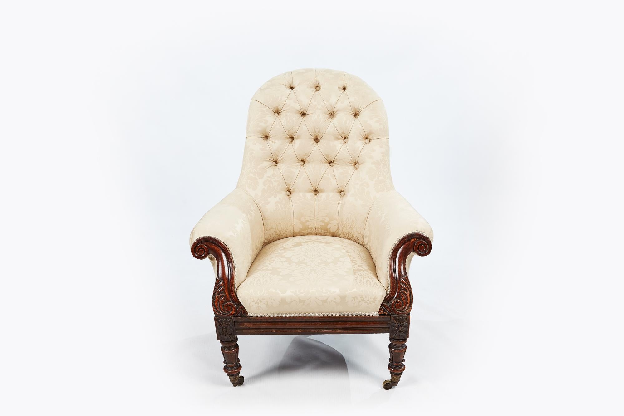 19th century pair of round-back upholstered armchairs. Dates from the transition period between square William IV lolling chairs and curvilinear Victorian; the carved embellishment typically Irish.