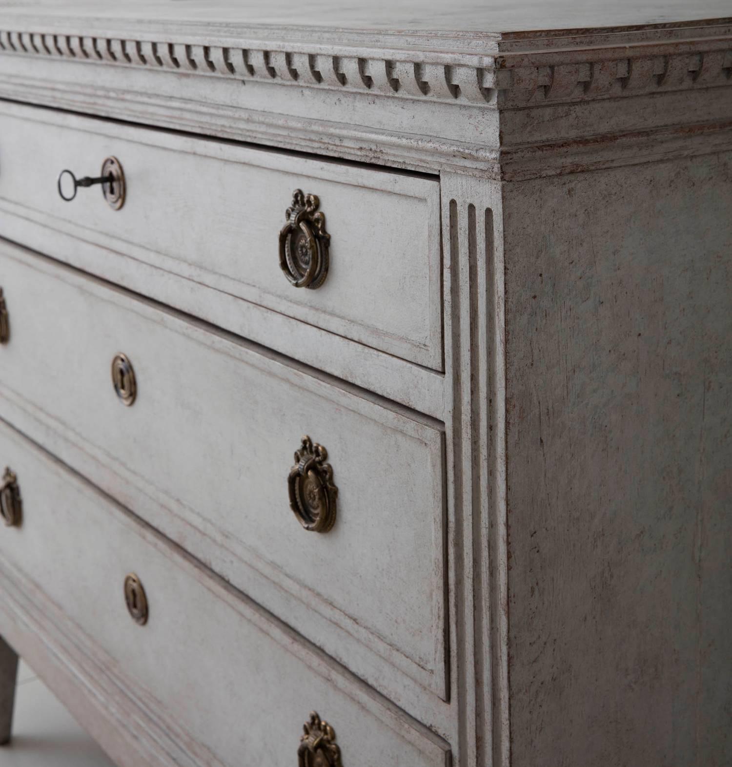 An elegant neoclassical pair of Swedish painted commodes in the Gustavian style. Each chest has three drawers, brass hardware, and original locks and keys. The hand-painted marbleized top is framed by dentil molding. The sides are fluted and the