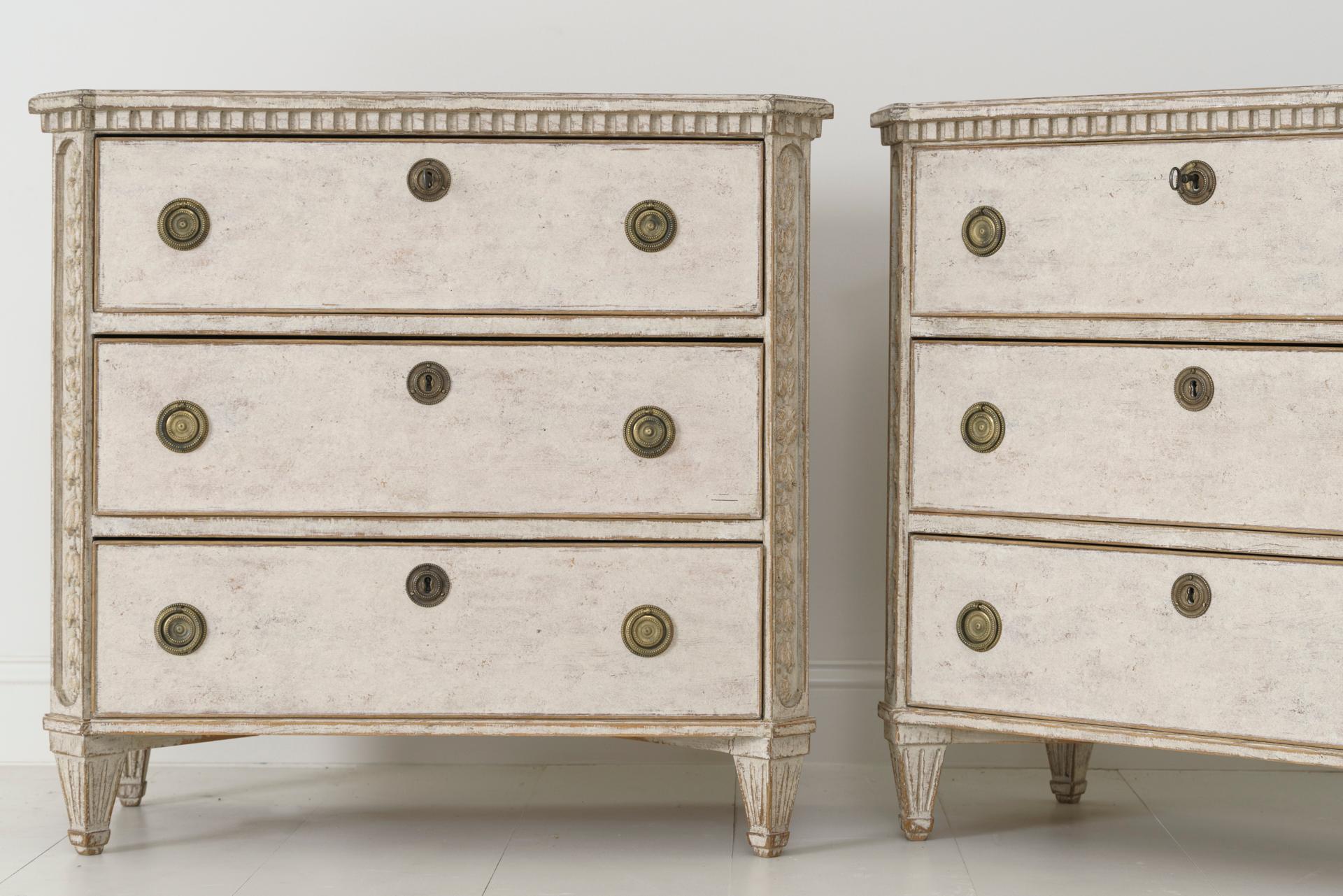 A pair of Swedish chest of drawers in the Gustavian style from the 19th century with dentil molding around the top and beautiful bell flower carvings on both the front and back corner posts. Tapered and fluted legs. The patina is a soft taupe with