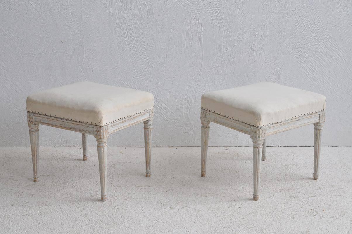 A pair of Swedish painted wood stools with upholstered seats covered in old muslin from the Gustavian period. These classically designed stools have fluted, turned legs. Chalky Gustavian aged-white paint finish.