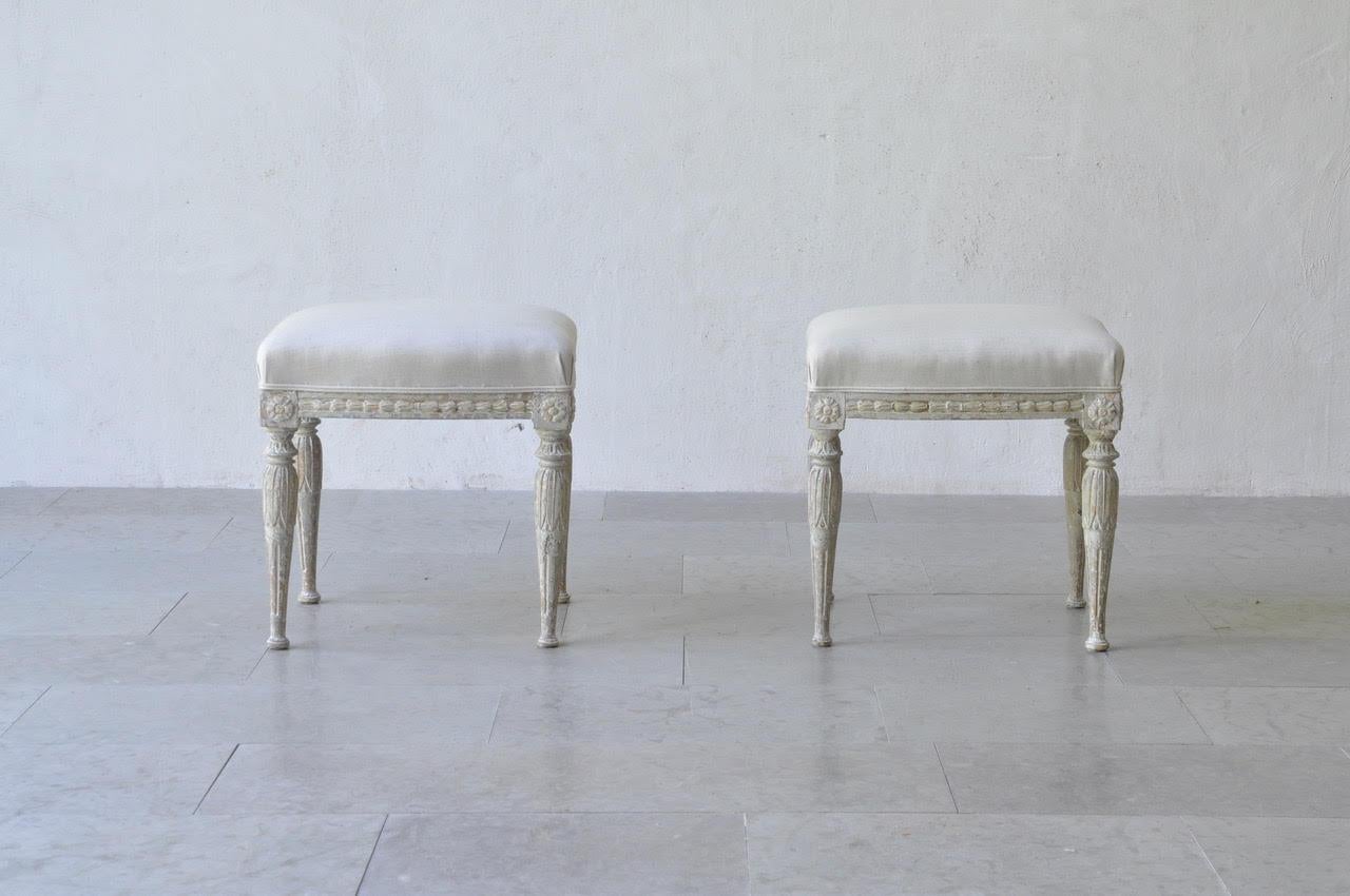 A beautiful pair of Swedish footstools from the Gustavian period. These stools have been hand-scraped to reveal the original paint. There are carved bell flowers on the seat frame with rosettes on the corner posts and acanthus leaves on tapered