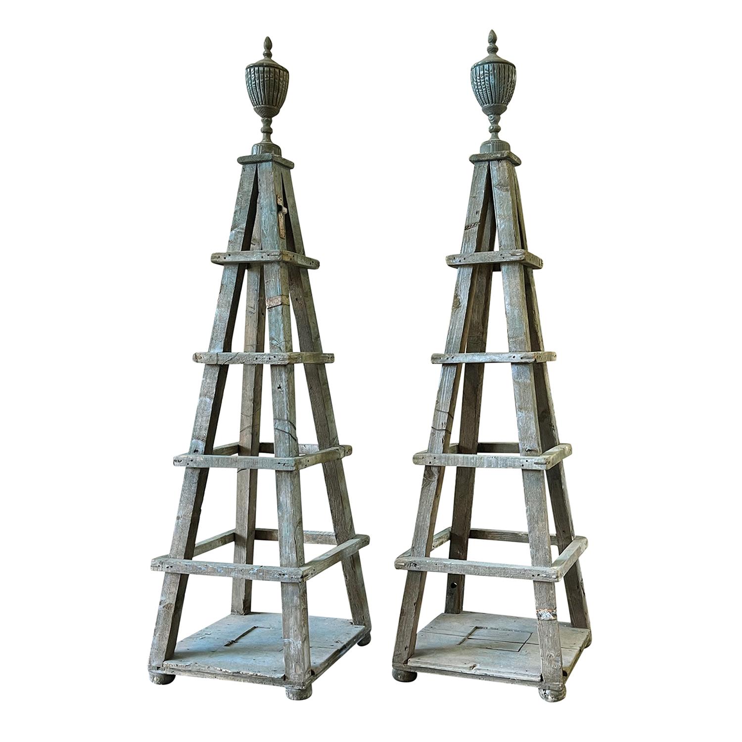 An antique French pair of tall garden trellis obelisks in faded Versailles green topped by urn finials, in good condition. An antique Architectural ornament for the indoors or outdoors. Made of hand carved Pinewood. Minor fading, due to age. Wear