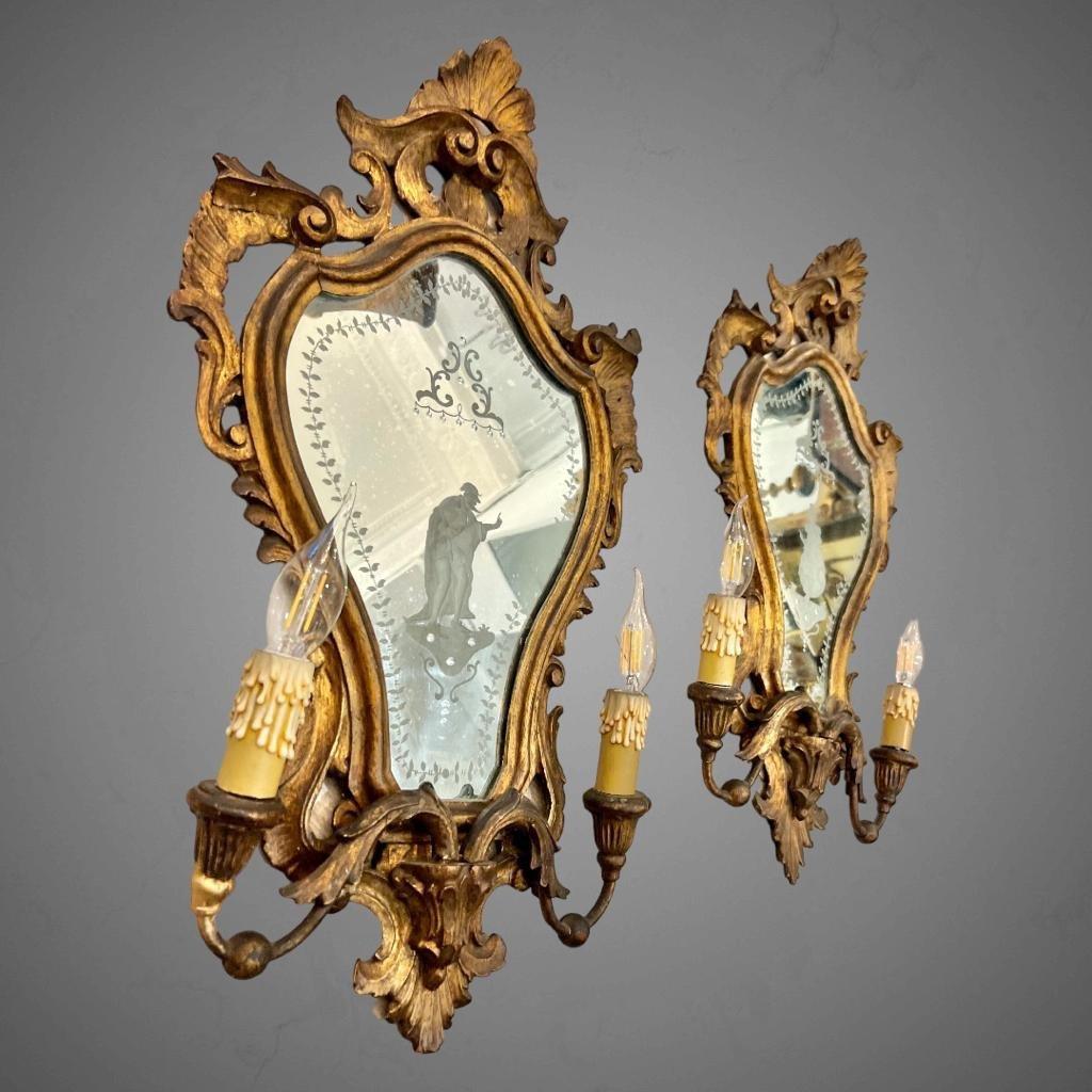 We present you this wonderful pair of Venetian sconces made from gilded wood, featuring beautifully engraved mirrored backgrounds. Crafted in the style of Louis XV and hailing from the late 19th century, these sconces come with two light fixtures