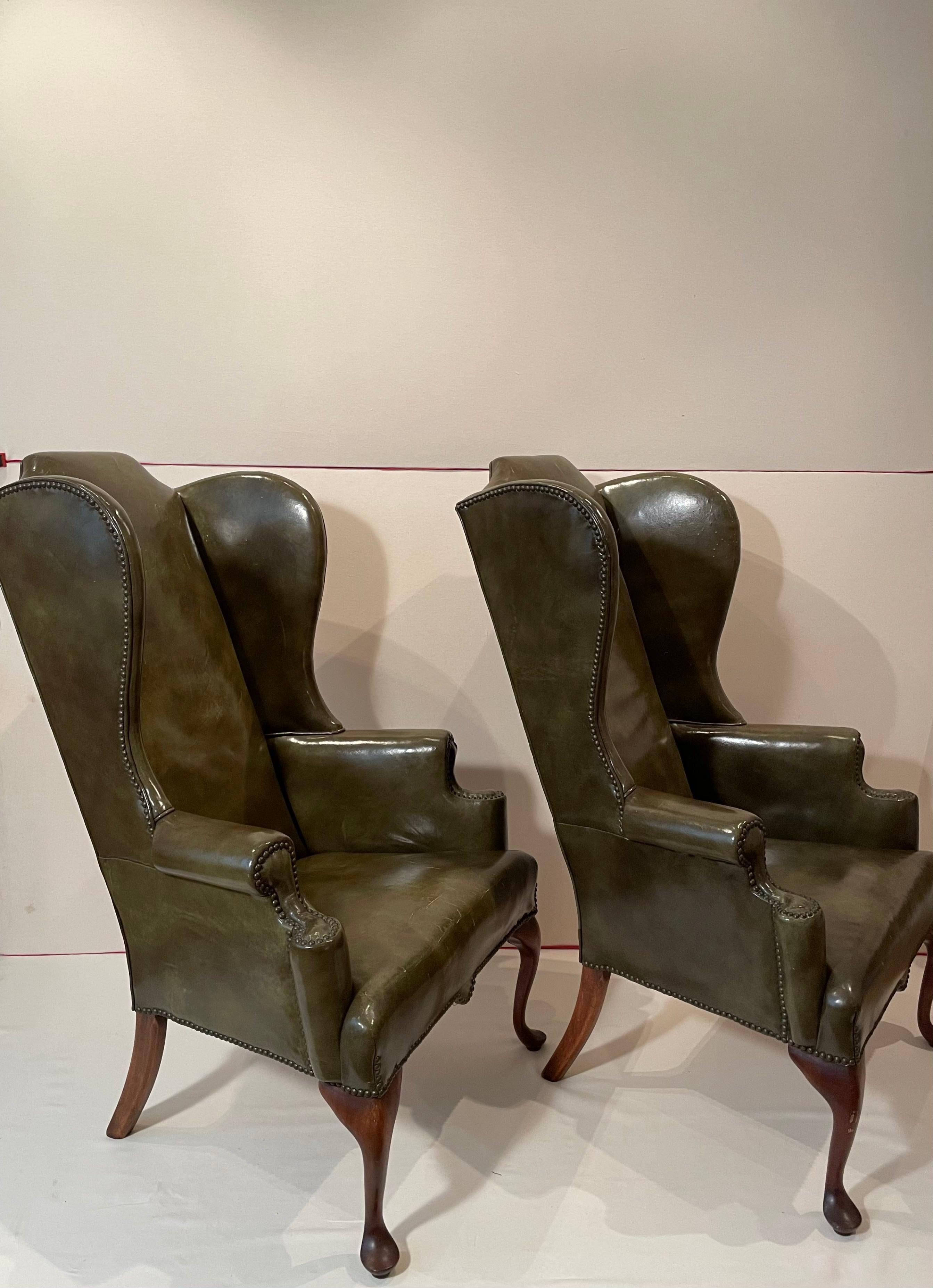 A lovely pair of Late 19th century English wingback chairs with walnut legs (Cabriole legs in the front and saber legs in the back), brass nail heads, and olive green upholstery by 