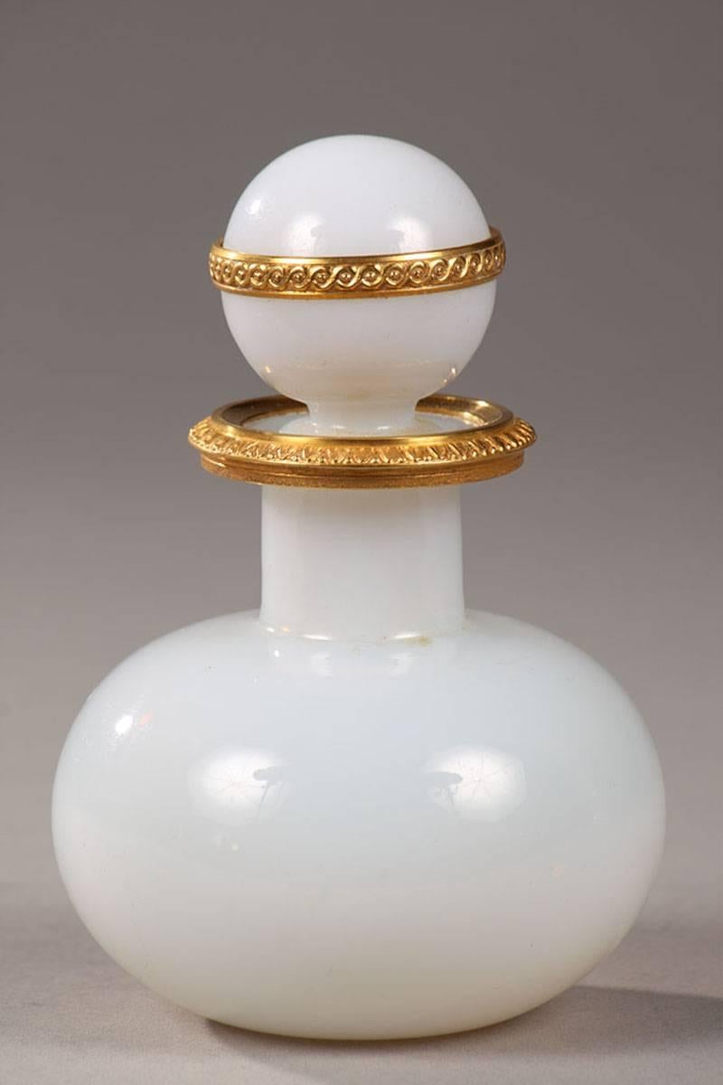 Pair of white, translucent opaline perfume bottles with their ball-shaped stoppers. The ormolu mounts are sculpted with a frieze of interlacing on the stopper and water leaves on the collar. The nuances of the white and the shape of the two bottles