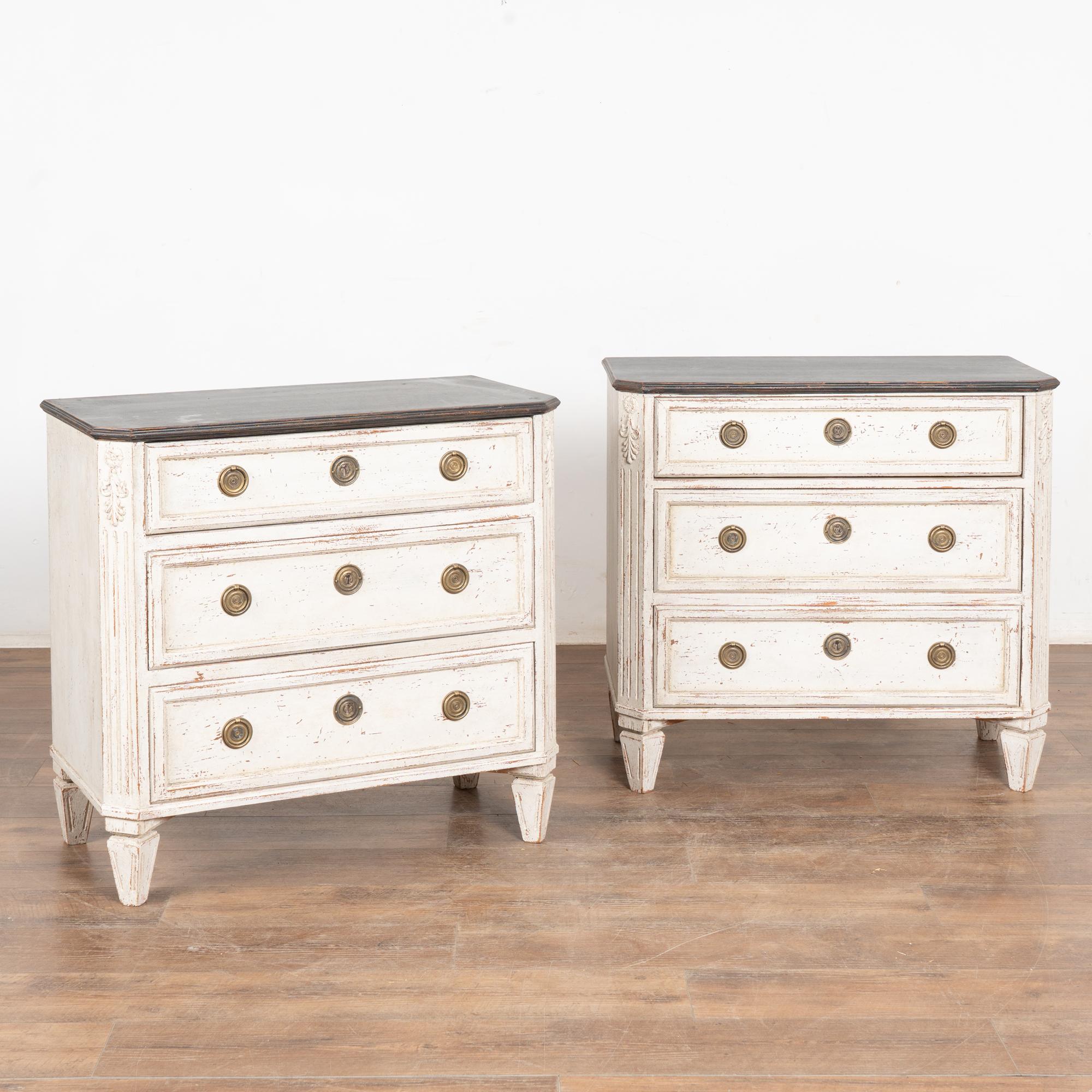 A pair of decorative pine Gustavian chest of drawers with canted fluted side posts with upper carved flourish, raised on four tapered fluted feet.
Restored, later professionally painted in layered shades of antique white with contrasting black top;