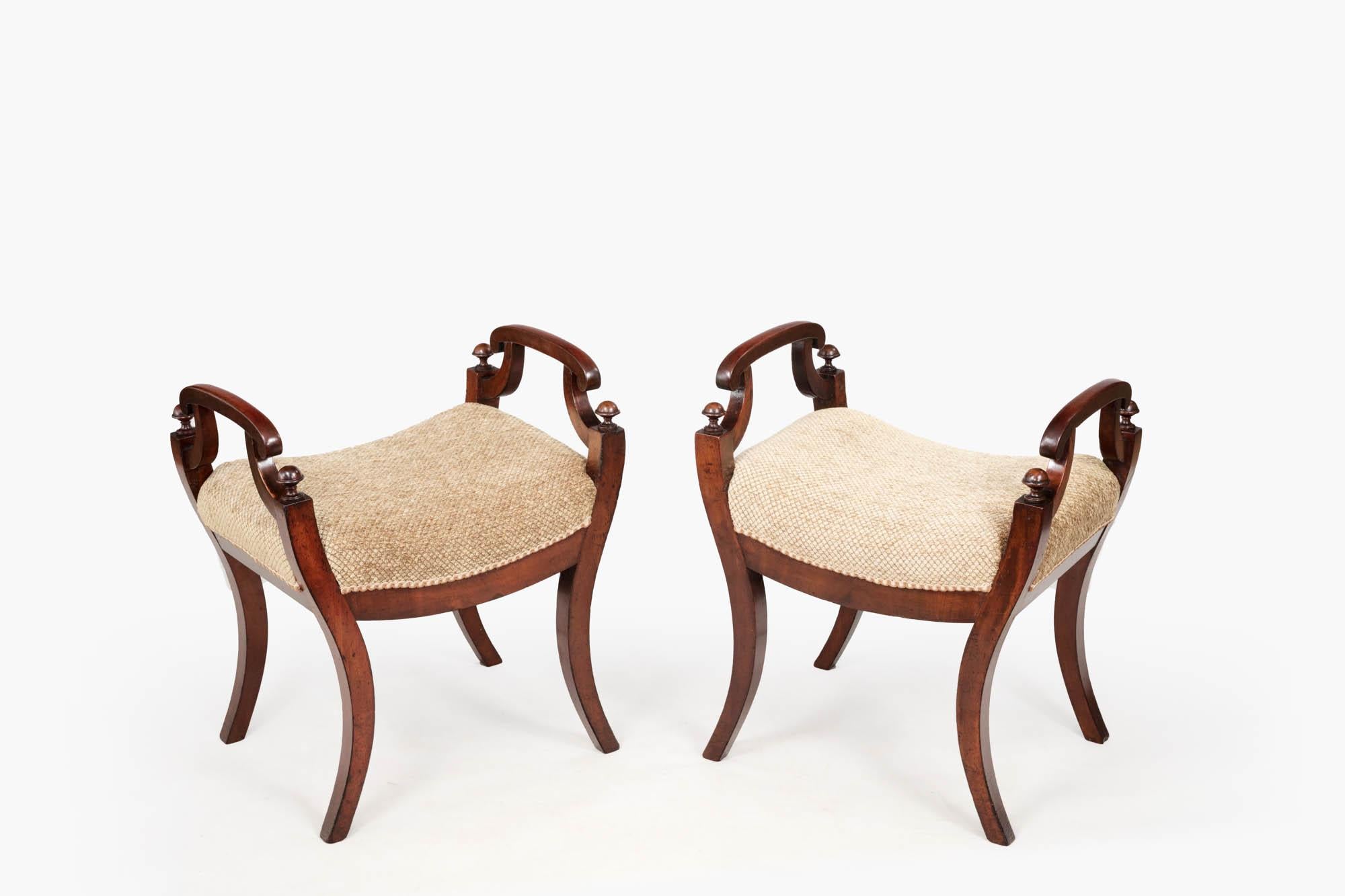 19th century pair of mahogany William IV twin-handled stools raised on simple sabre legs topped with rounded, carved finals. The seats have recently been re-upholstered in a buff-coloured fabric with braiding to the edges where it joins the wood.