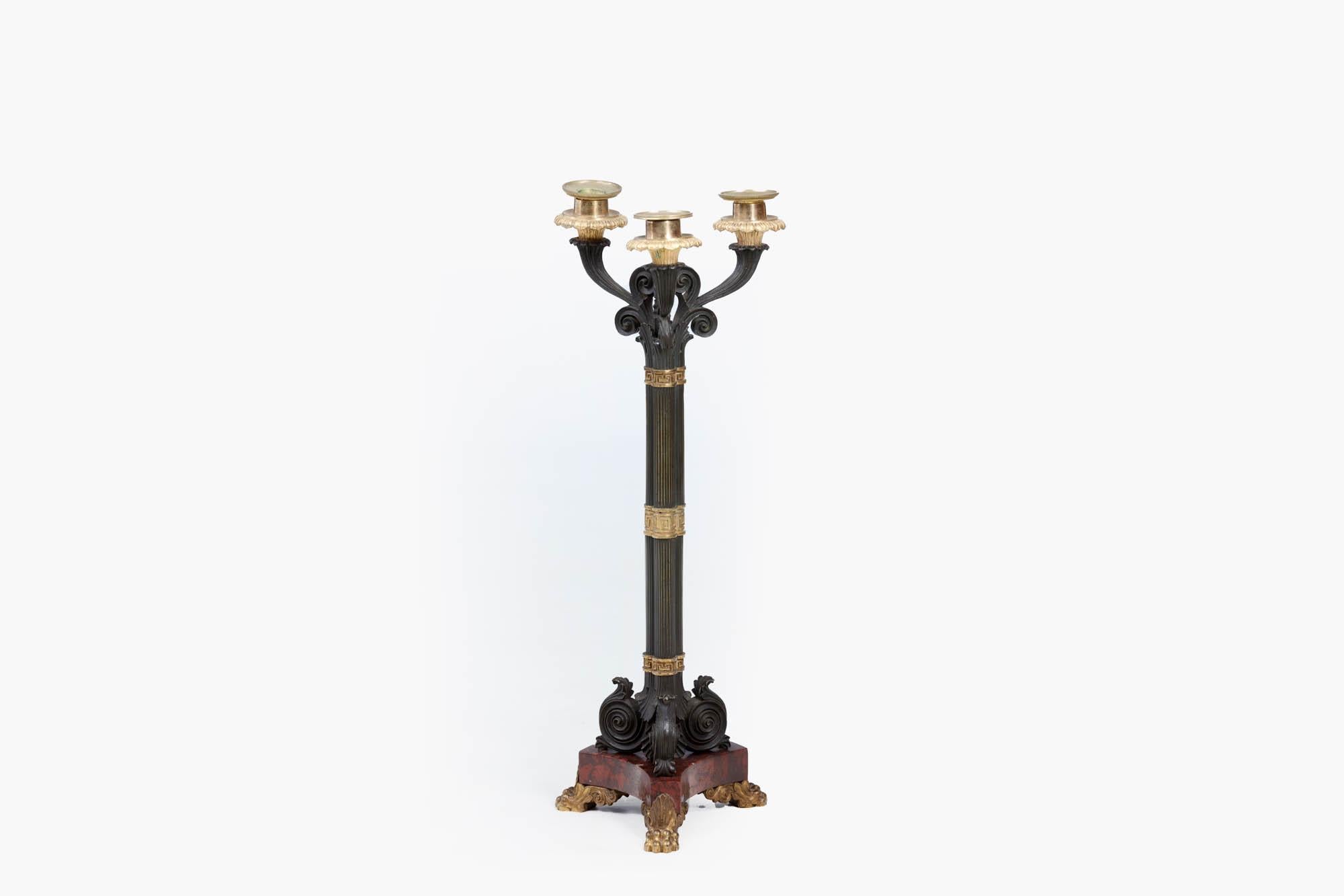 19th century pair of Regency bronze three light candlesticks, in the Classical style, patinated with gilt highlights, and featuring Greek cut key banding. The reeded naturalistic pillars rise upwards to the three branches of the candelabra with