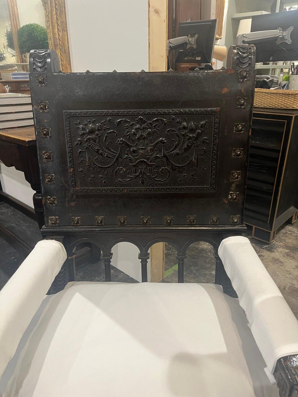 Pair Spanish Revival Chairs Hand Carved with Embossed Leather seats and backs. Intricately carved scrolls, arched spindles and stretchers. large pyramid shaped trim. Leather has Lion's mask motifs Cushions are removable, and arm covers have Velcro