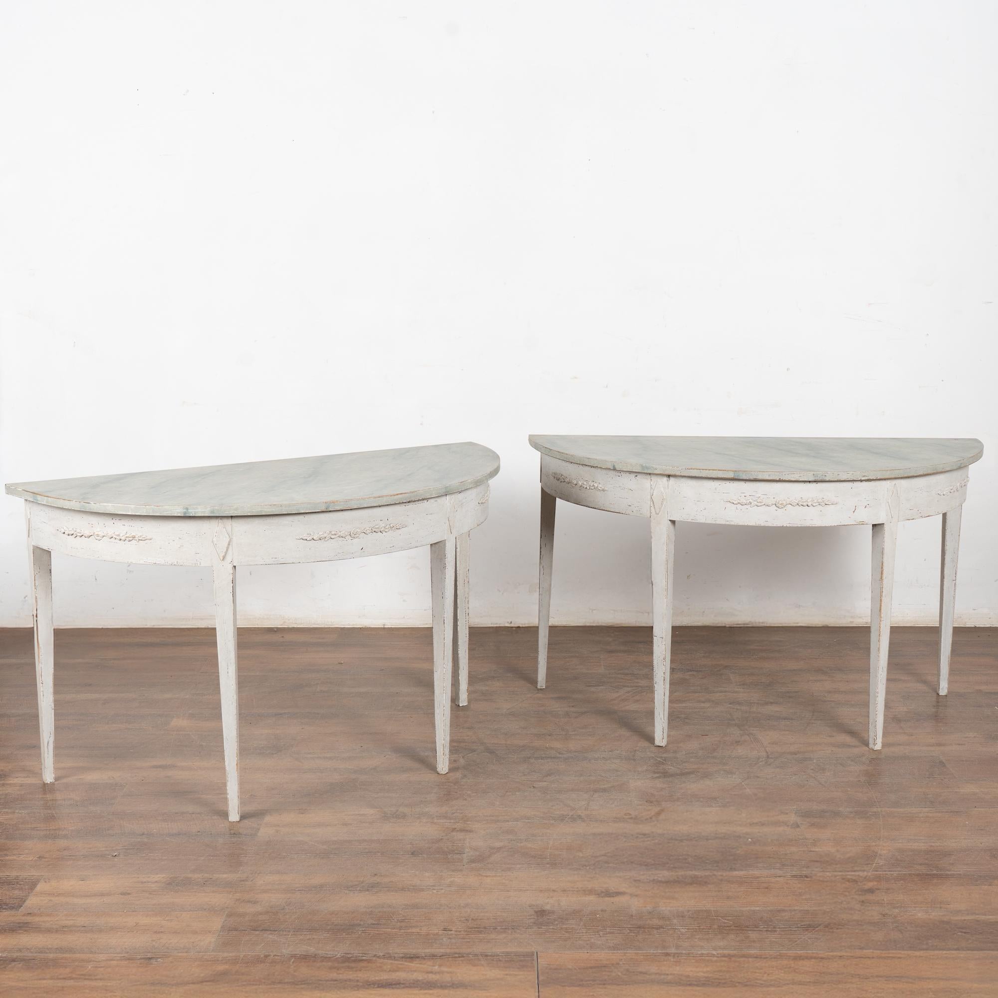 Pair, gustavian demi-lune side tables or consoles. 
Gently tapered fluted legs and skirt with applied carved floral swag.
Newer professionally applied layered antique white painted finish, slightly distressed to fit age and grace of the tables. Top