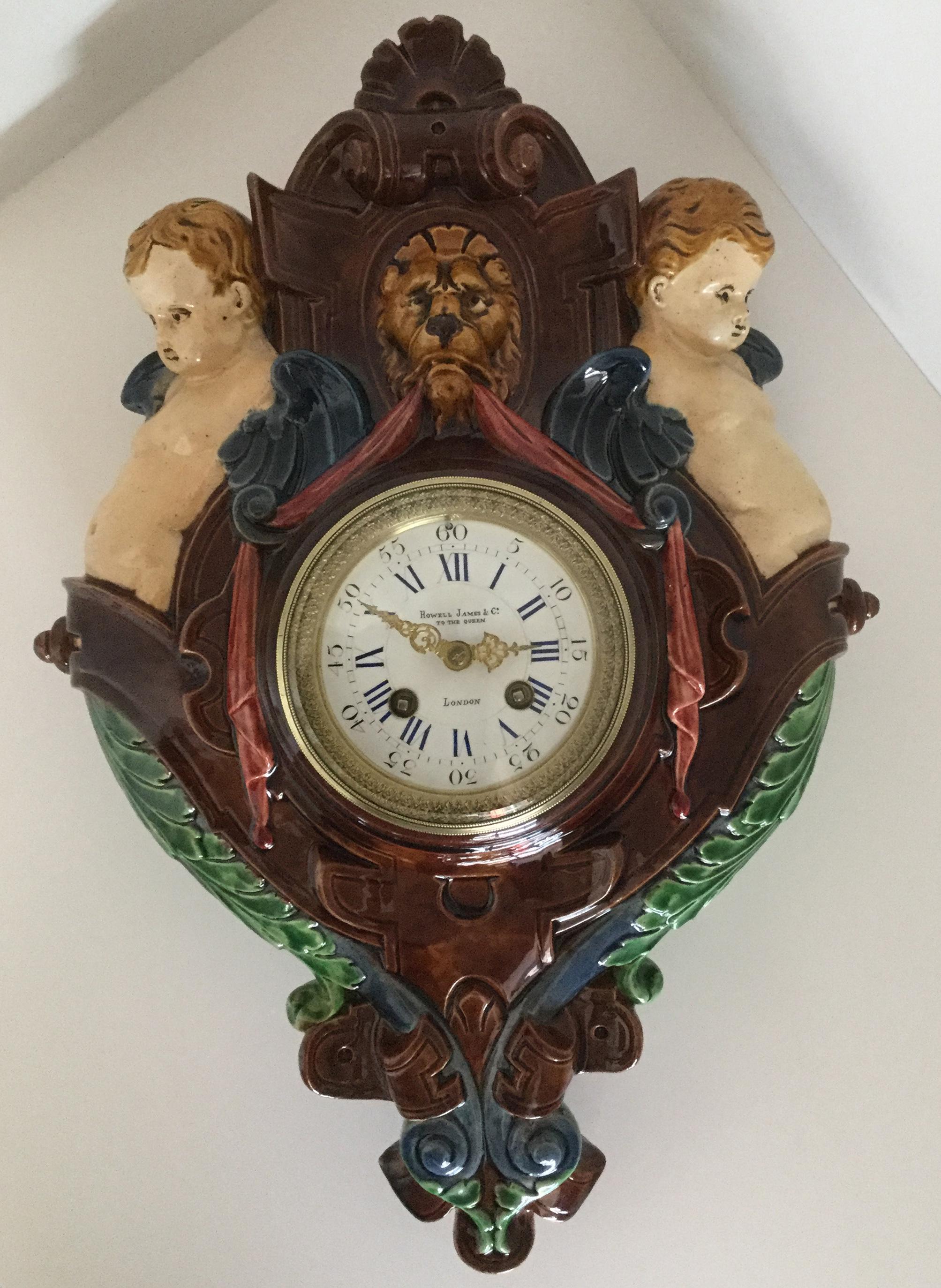 A very rare decorative Palissy Ware Majolica 8 day striking wall clock, circa 1870, on multicolored ground, with green, cream, red, blue and brown decoration, surmounted by a lions head flanked by twin putti, with ribbon, leaf and scroll decoration,