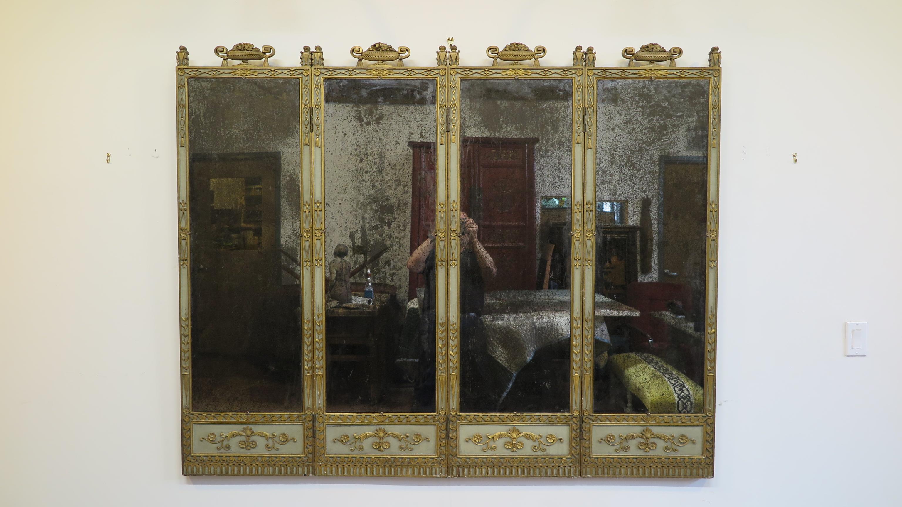 A 19th century Italian mirror panel. 19th century panel screen mirror. Four Paneled screens of carved, painted, and gilded gesso over wood. Each section eloquently adorned surmounted by flower filled flaming burst Tureens over a rectangular frame