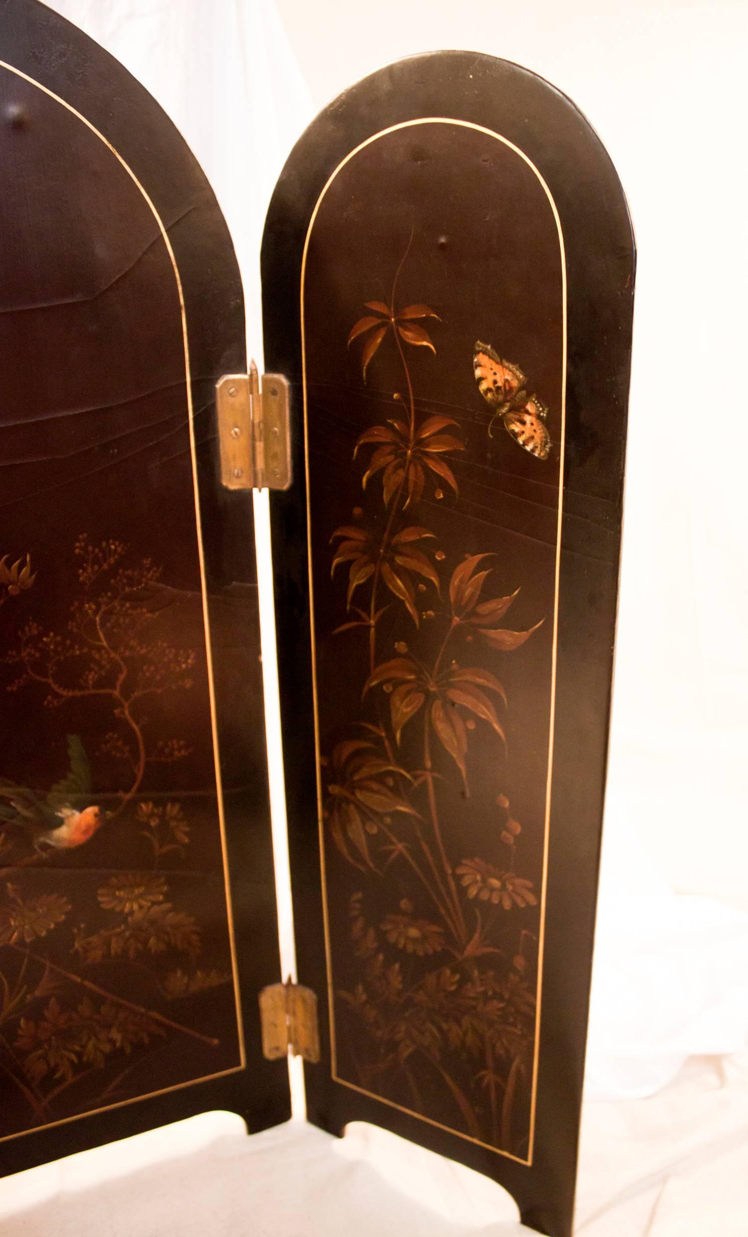 Unusual small size papier mache tabletop screen featuring hand painted flowers, a colorful bird and butterfly. Three brass hinged panels. Half round shaped top of panels with two plain bracket feet on each panel. See measurements below.