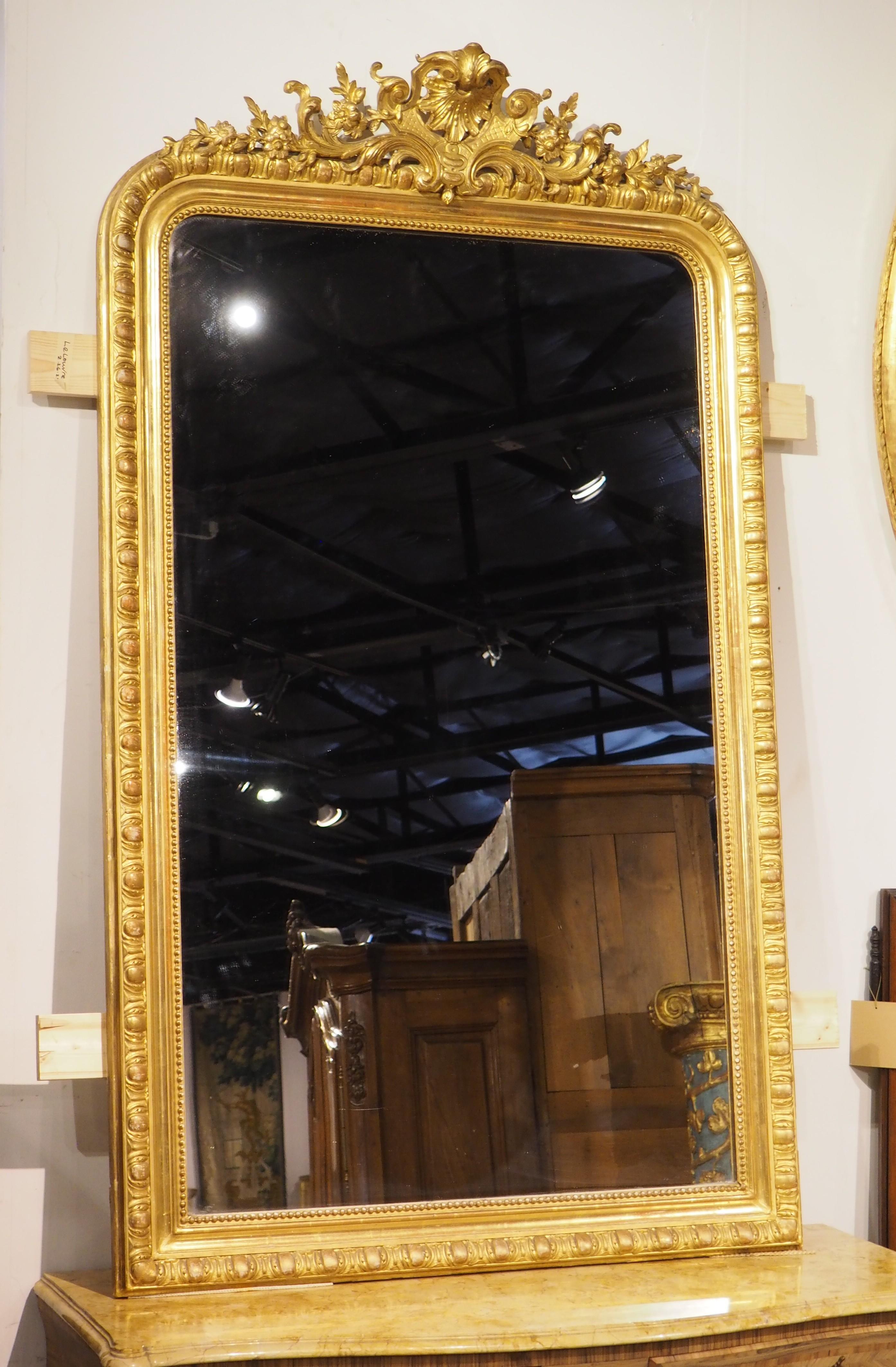 The carvings of this Parisian giltwood mirror are quite impressive, highlighted by the sprawling crest inspired by nature. Hand-carved circa 1880, the motifs of the golden frame are indicative of the style of Napoleon III. Napoleon III, also known