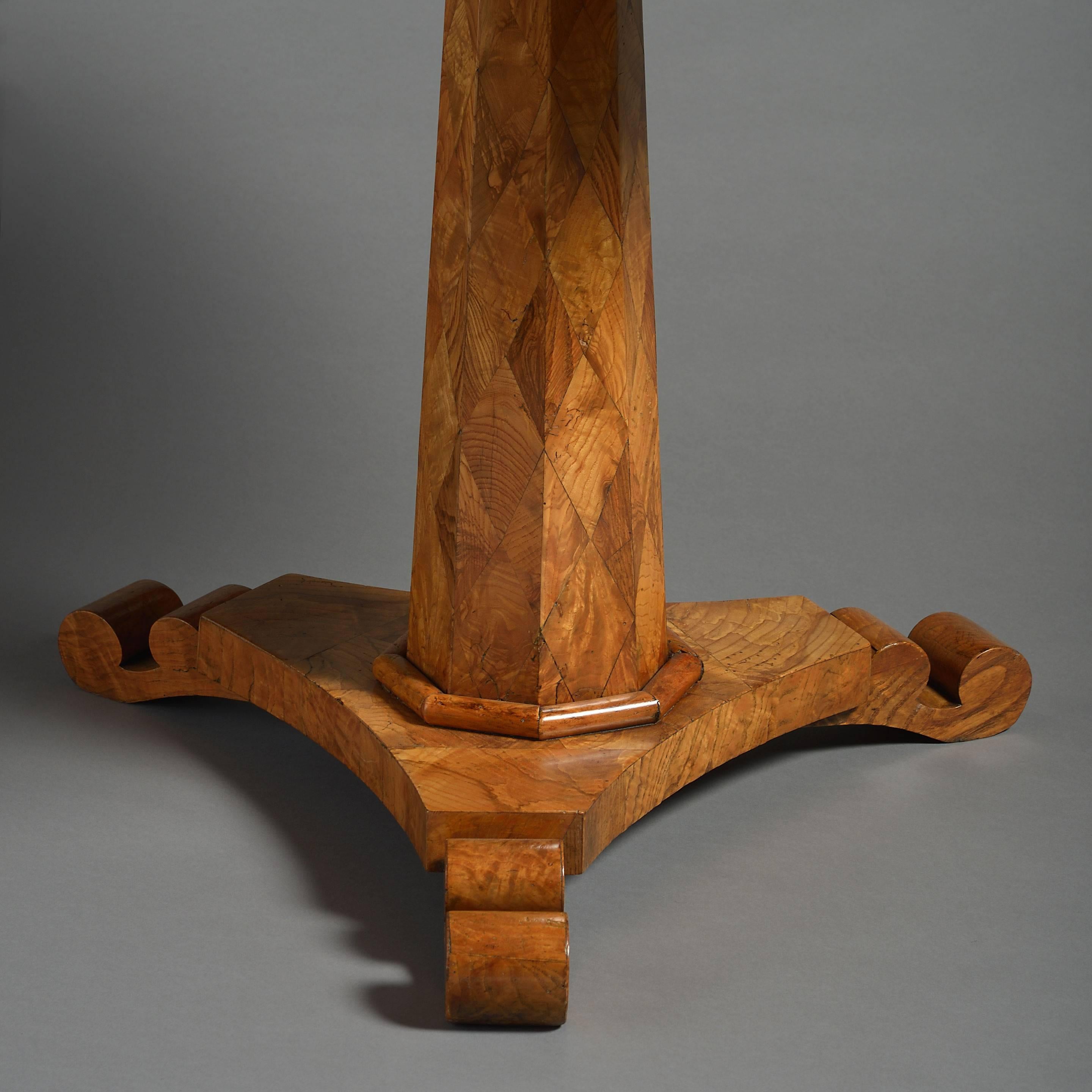 A mid-19th century elm parquetry occasional table, the patchwork veneered top set upon an octagonal tapering stem of the same and terminating in a plinth base with three scrolling feet.