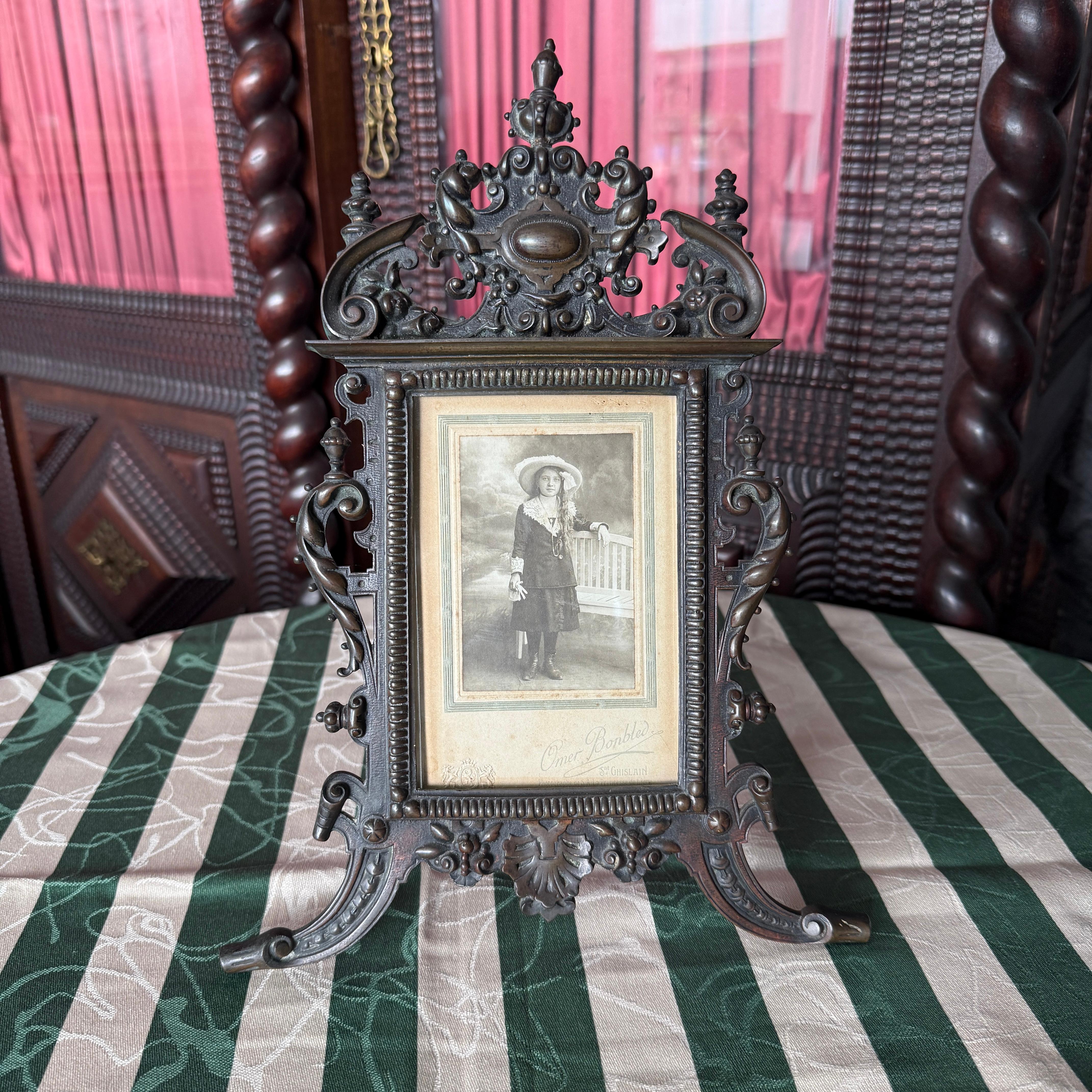 This exquisite 19th Century patinated bronze picture frame is a striking example of refined European craftsmanship from the Victorian era. Elaborately cast in rich detail, the frame features an ornate openwork design that combines classical motifs