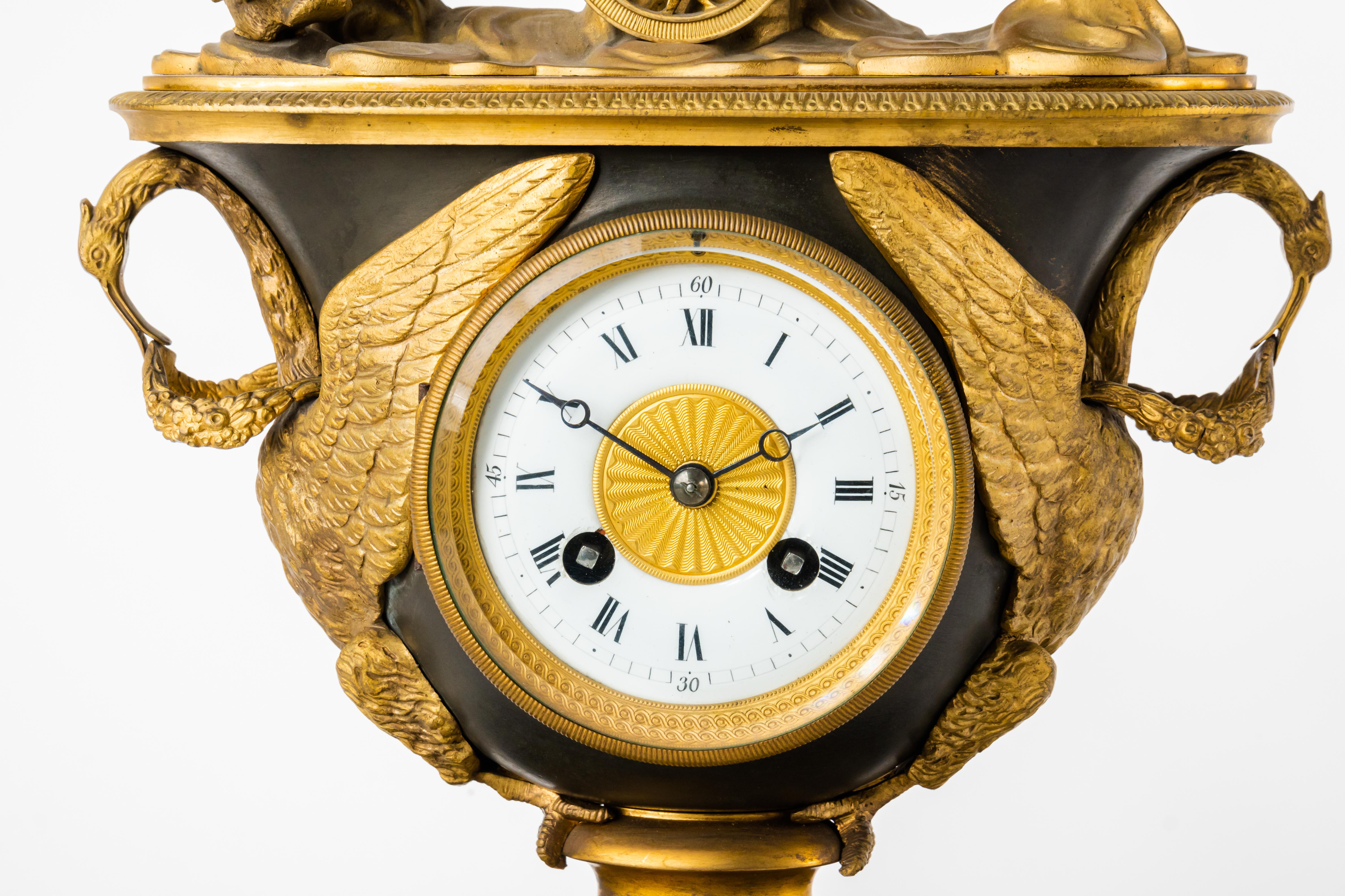A patinated & gilt bronze empire striking mantel clock set pendule Au Vase. France Circa 1810.

The case modeled as a vase with swan handles topped by Cupid in a chariot drawn by cockerels, on oval plinth, with white enamel dial.

Clock: 15½ in.