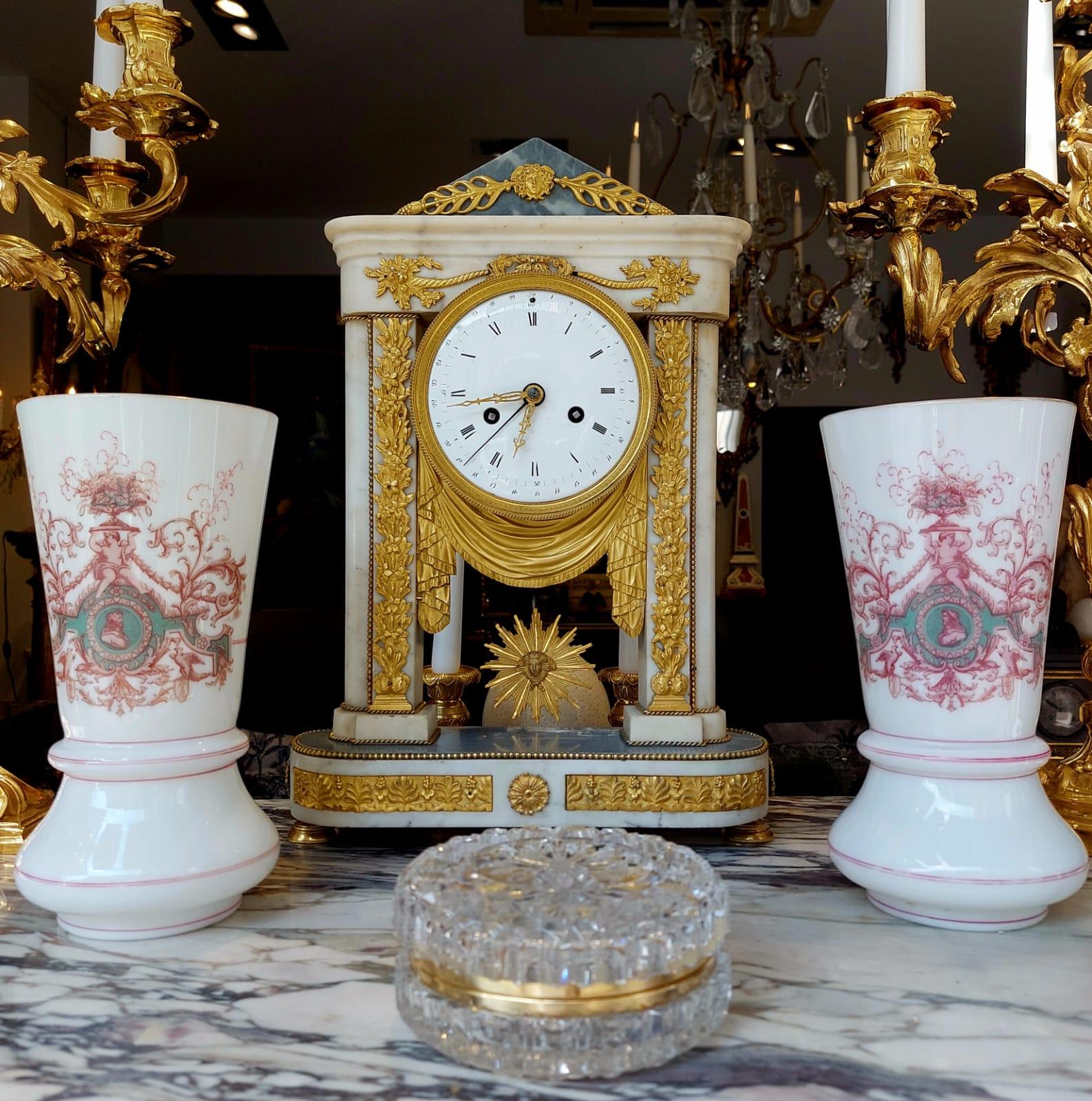 Empire period portico clock in white marble and gilt bronze, 19th century

This Empire period clock (circa 1800-1810) is composed of a marble terrace topped by two flat columns decorated with a frieze of acanthus leaves in gilt bronze and doubled at