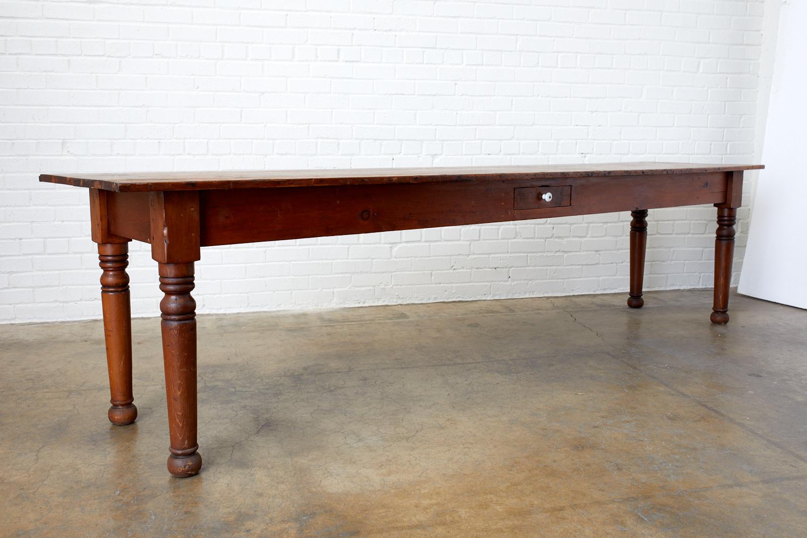 Large, rustic 19th century Pennsylvania Dutch American farmhouse table, harvest table, or work table. Features a nearly 10 foot long plank top that appears to be pine supported by thick turned legs with ball feet. The tables has a storage drawer in